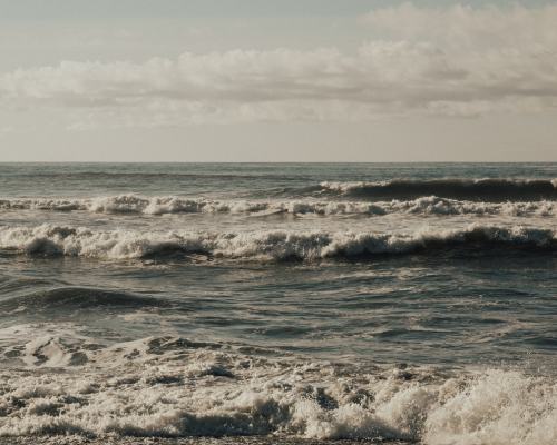 Ocean waves crashing on the shoreline under a partly cloudy sky.