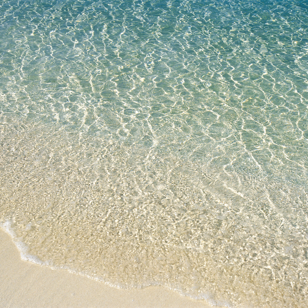 Clear ocean water lapping onto sandy beach with ripples in water.
