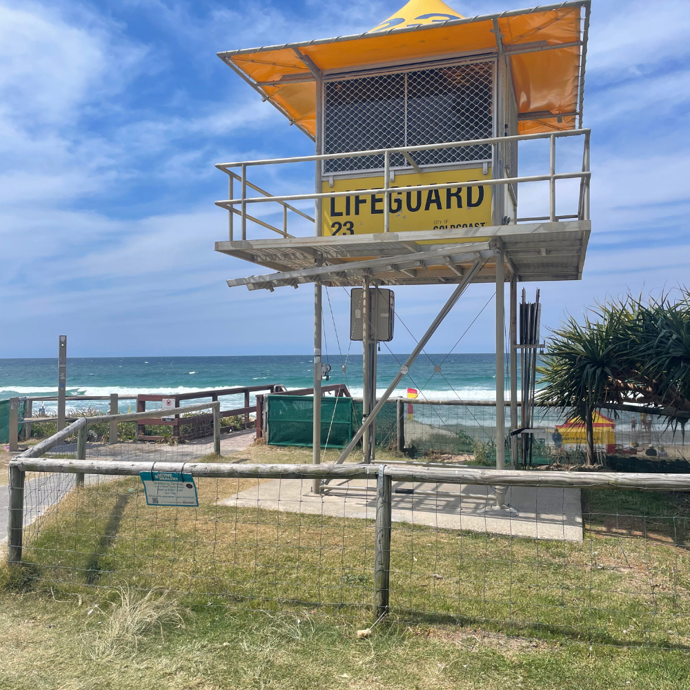 A yellow lifeguard tower with a small balcony on a beach, overlooking the ocean, under a clear blue sky.
