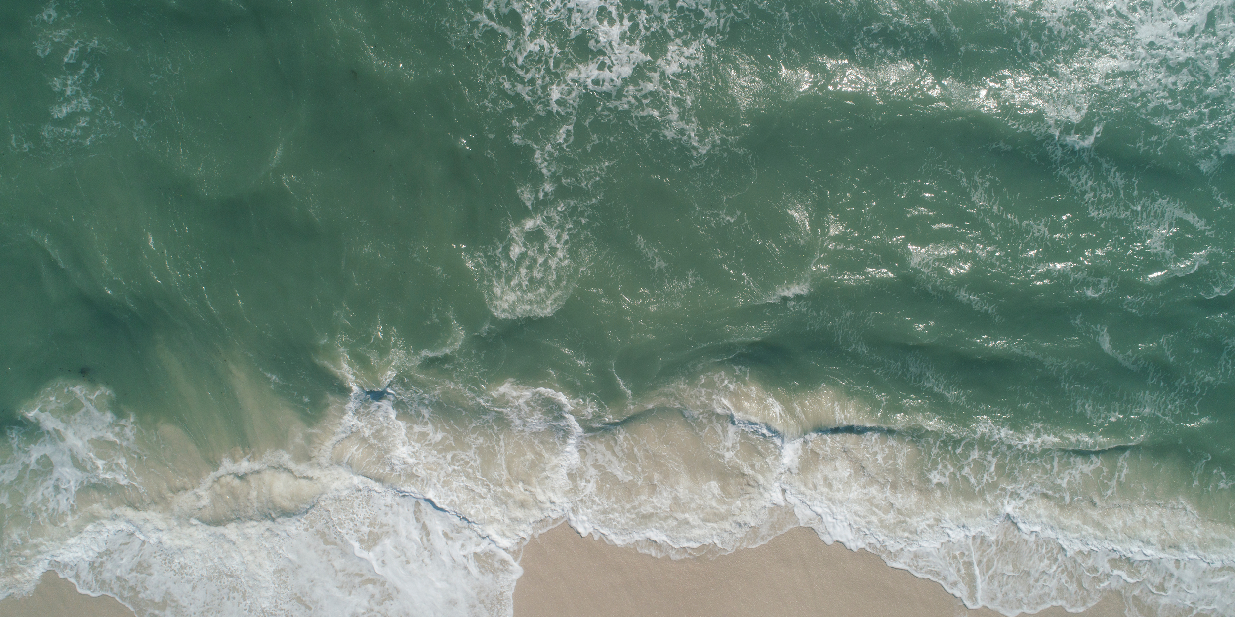 Aerial view of the shoreline with ocean waves crashing onto sandy beach.