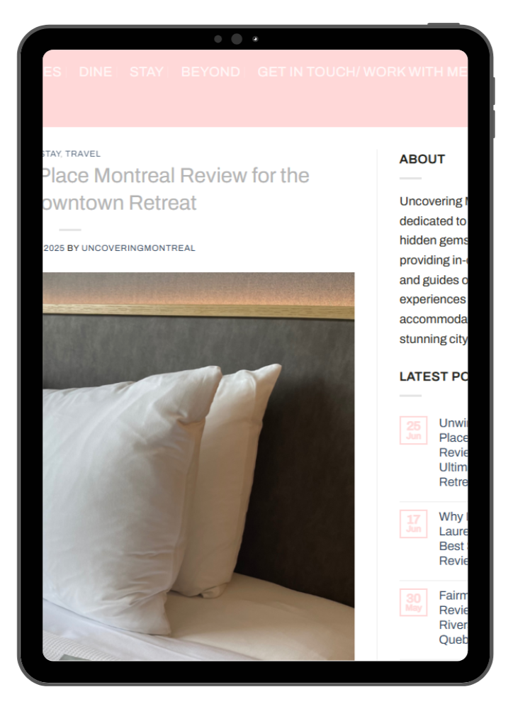 Close-up of a bed with white pillows and bedding in a hotel room, with a website displayed on a tablet screen in the background.
