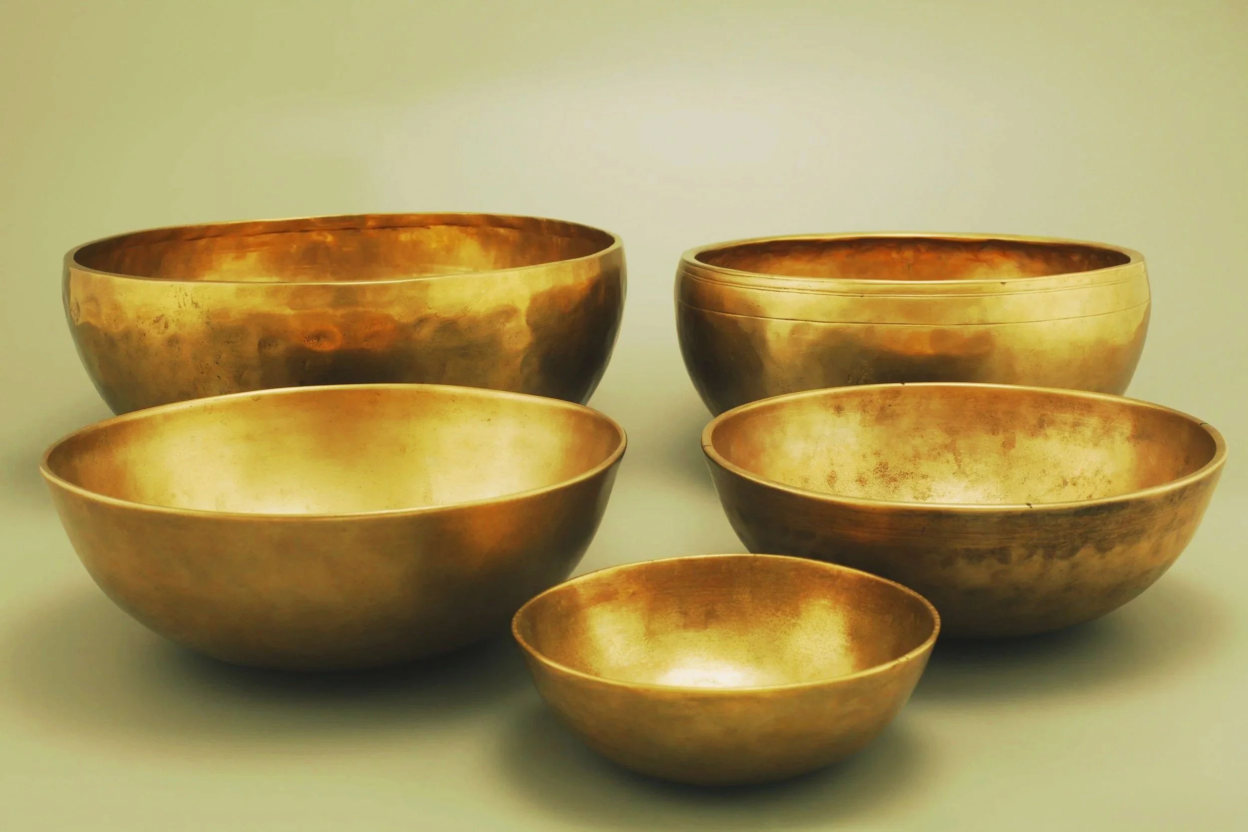 Multiple singing bowls illuminated by candlelight on a dark wooden surface with various musical mallets and a small lit candle.