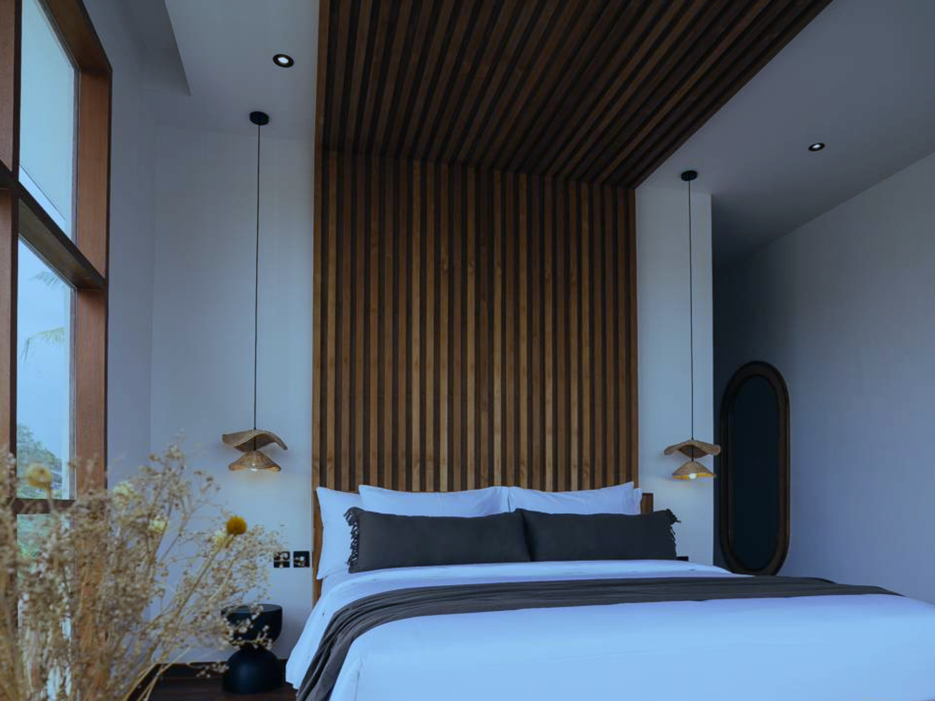 Modern bedroom with white bedding, black pillows, and a wooden accent wall, illuminated by hanging pendant lights.