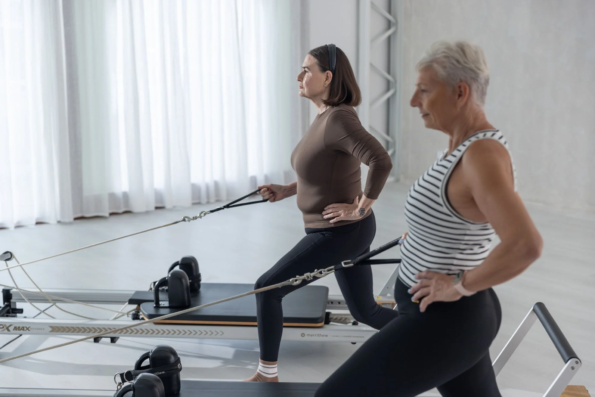 Women participating in a Pilates or physical therapy session using reformer machines in a modern studio.