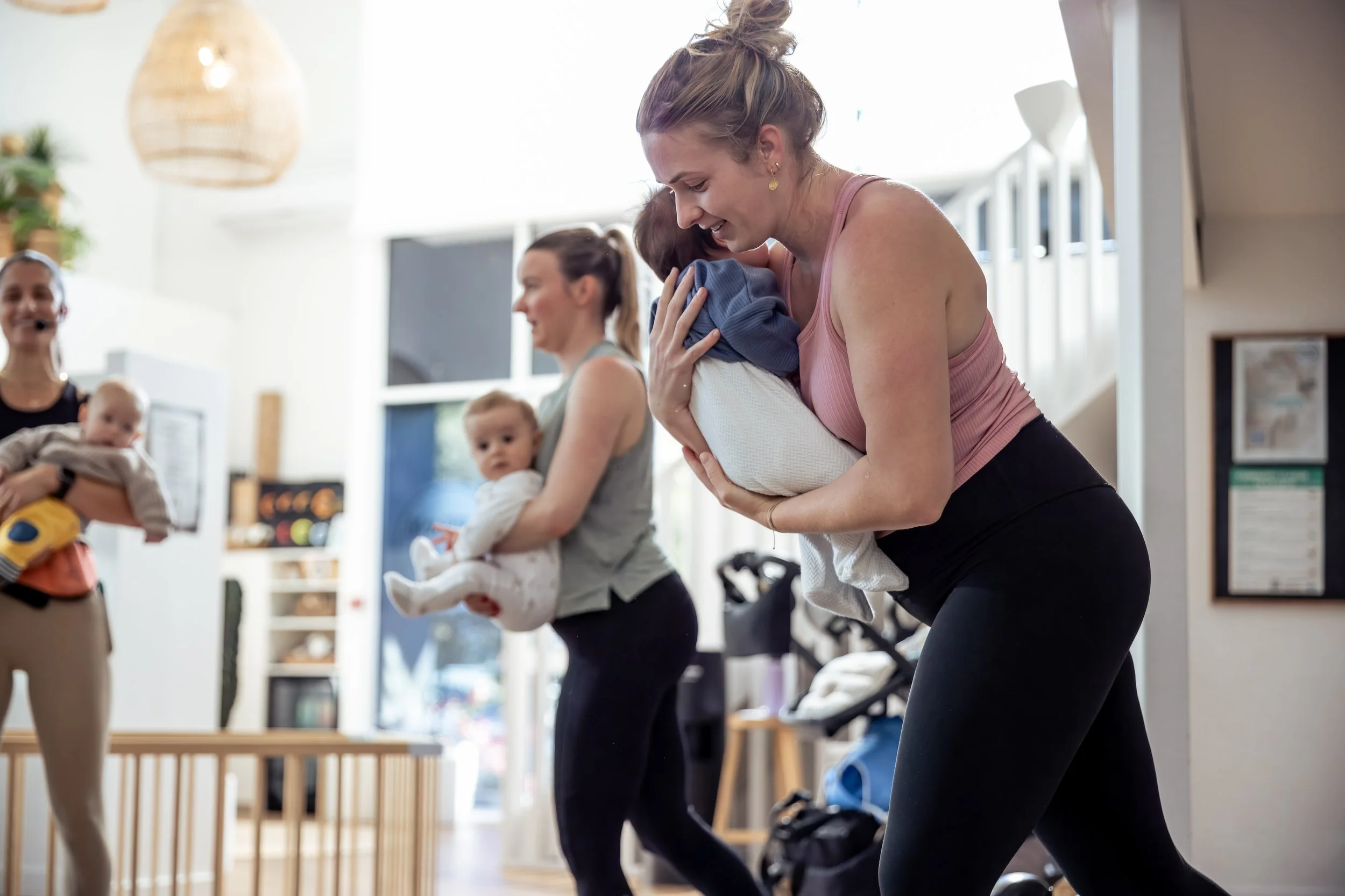 Women participating in a fitness class with babies in some of their arms, smiling and engaging in the activity.
