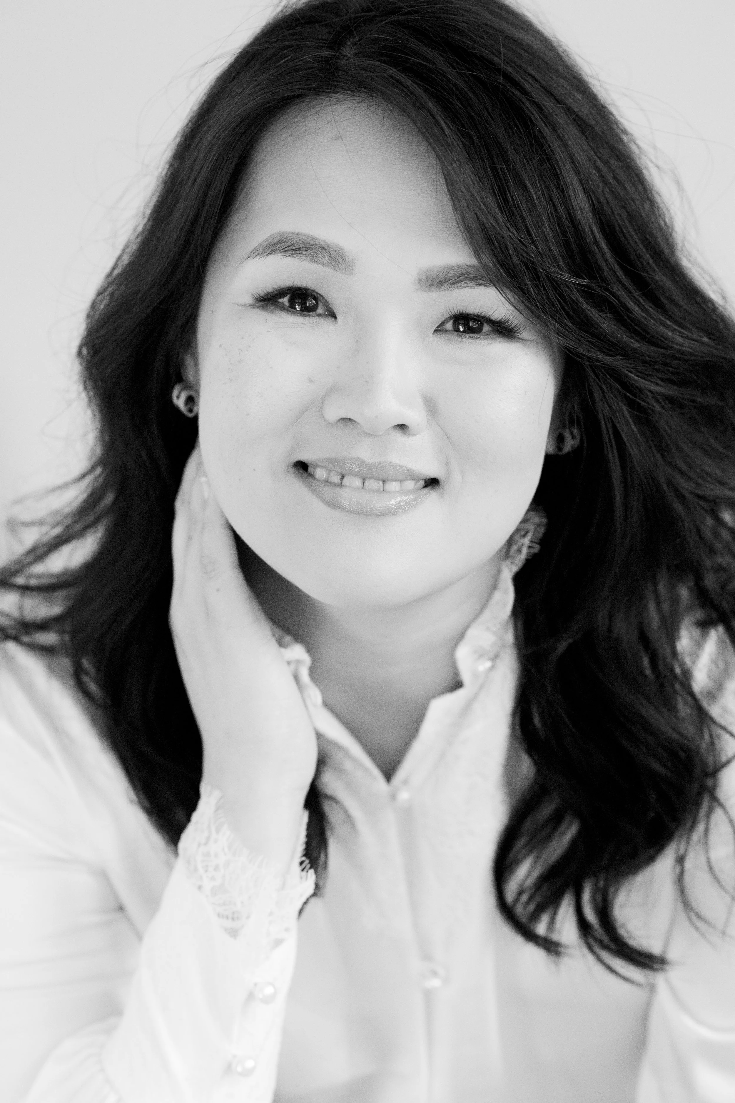 Black and white portrait of a woman smiling, with shoulder-length wavy hair, wearing earrings and a light-colored blouse.