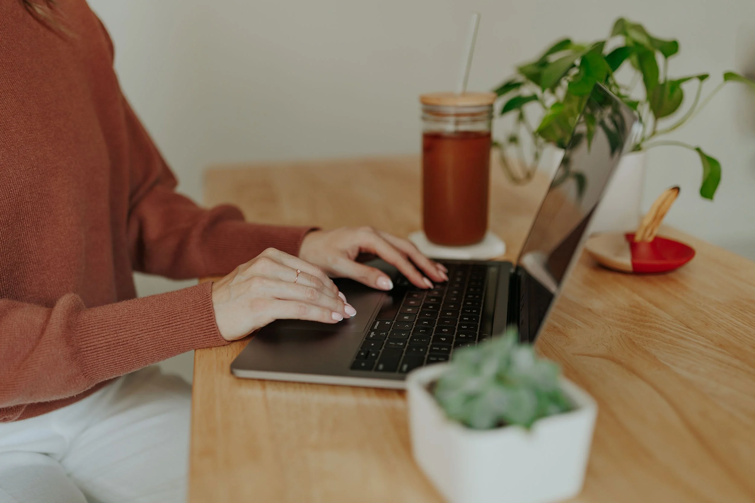 A woman typing on her computer with a honey colored jar and plants in the background