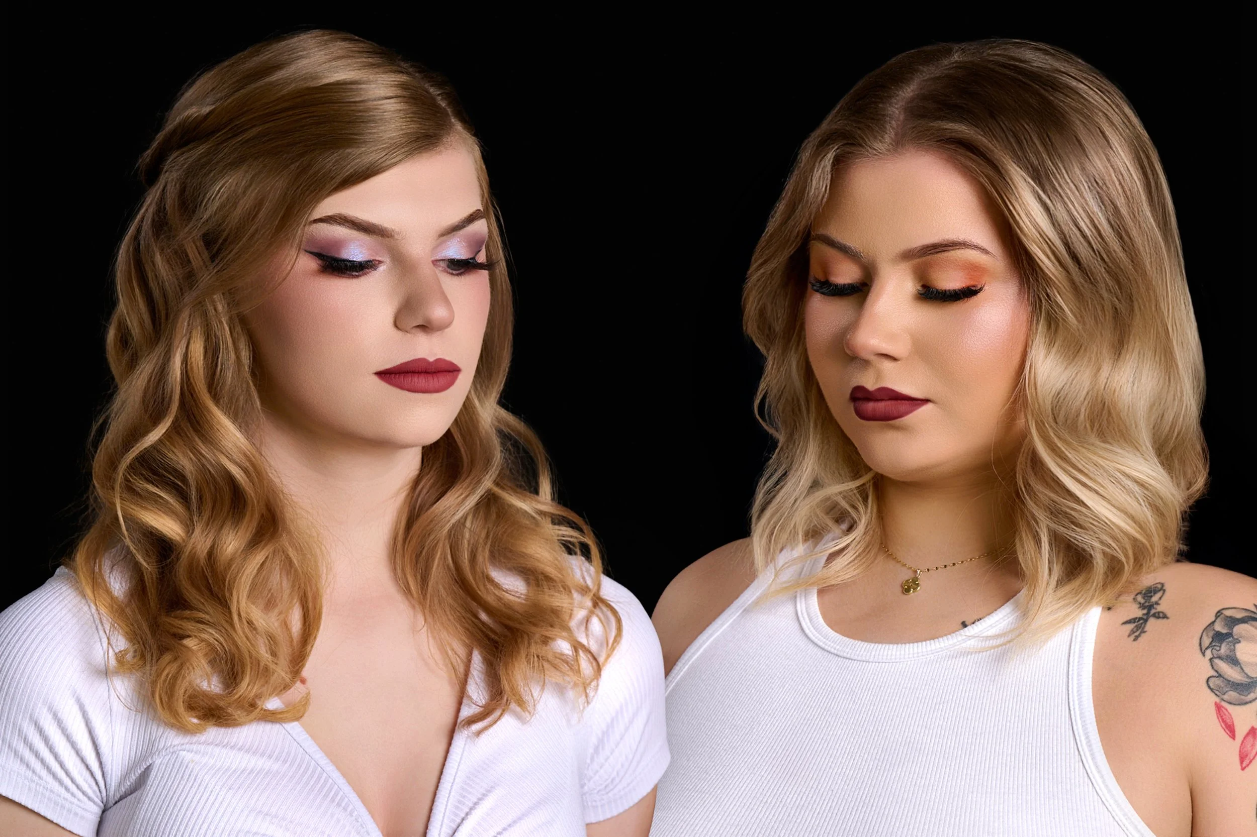 Two women with blond wavy hair and makeup standing close together against a black background, wearing white tops.