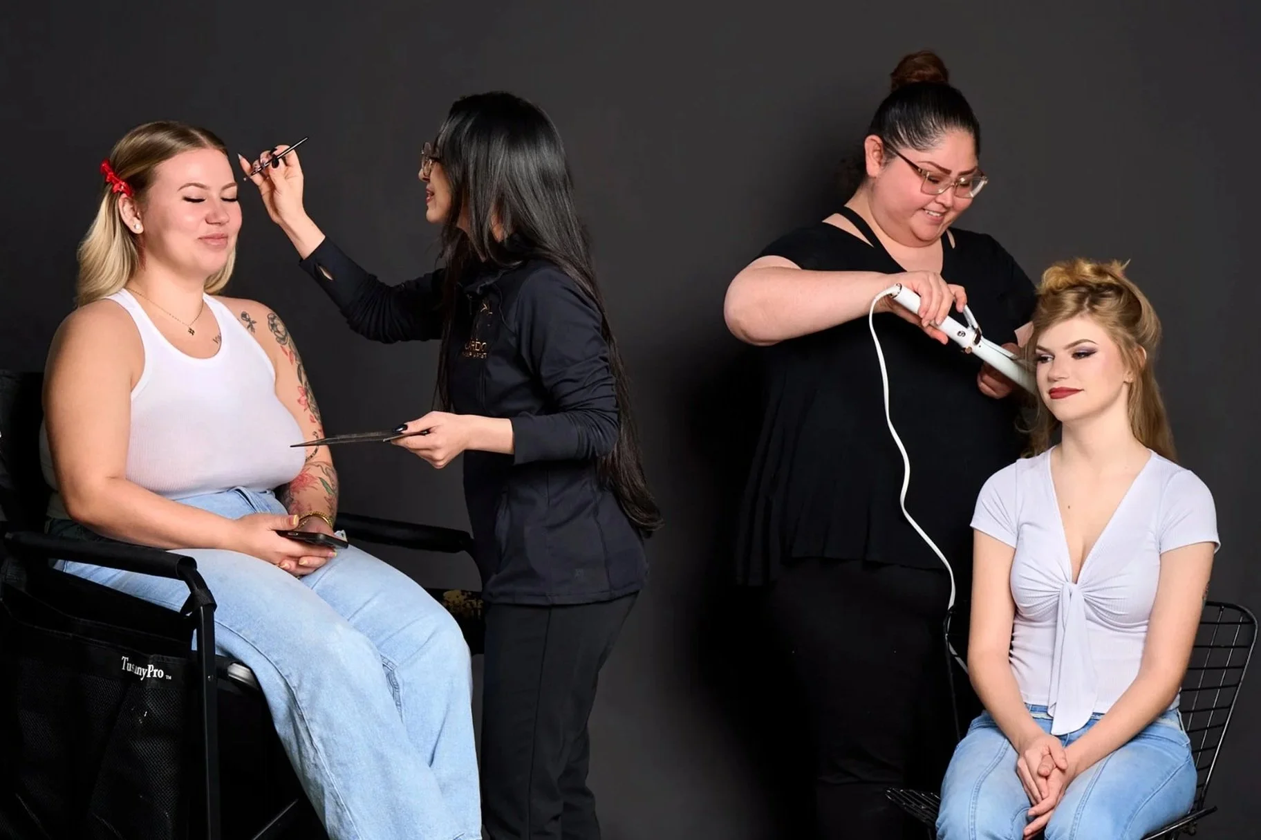 Two women getting their makeup and hair done at a photo studio with a black background.