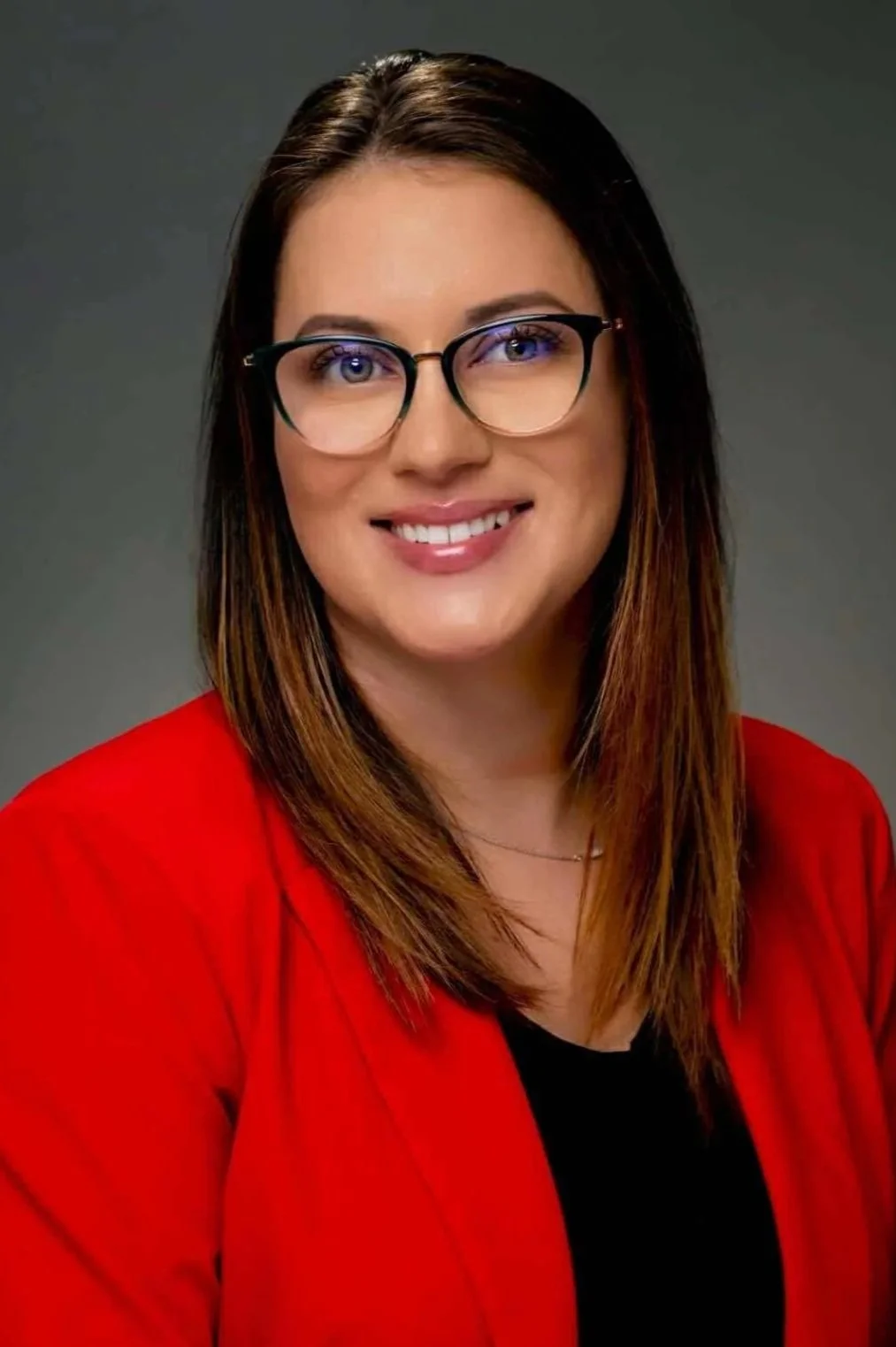 A woman with shoulder-length brown hair wearing glasses, a red blazer, and a black top smiling at the camera.