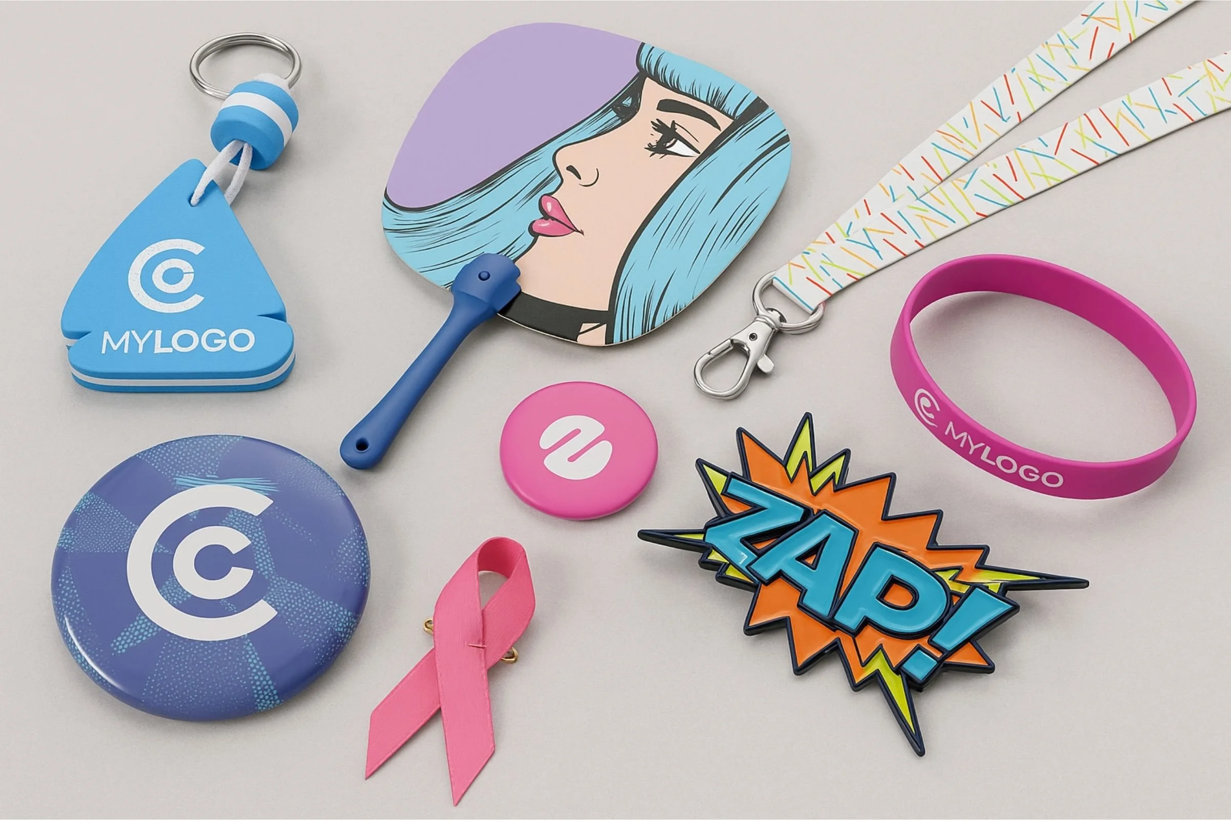 Sélection de goodies personnalisés : badges, porte-clés, tour de cou, bracelet et pin’s sur fond clair.