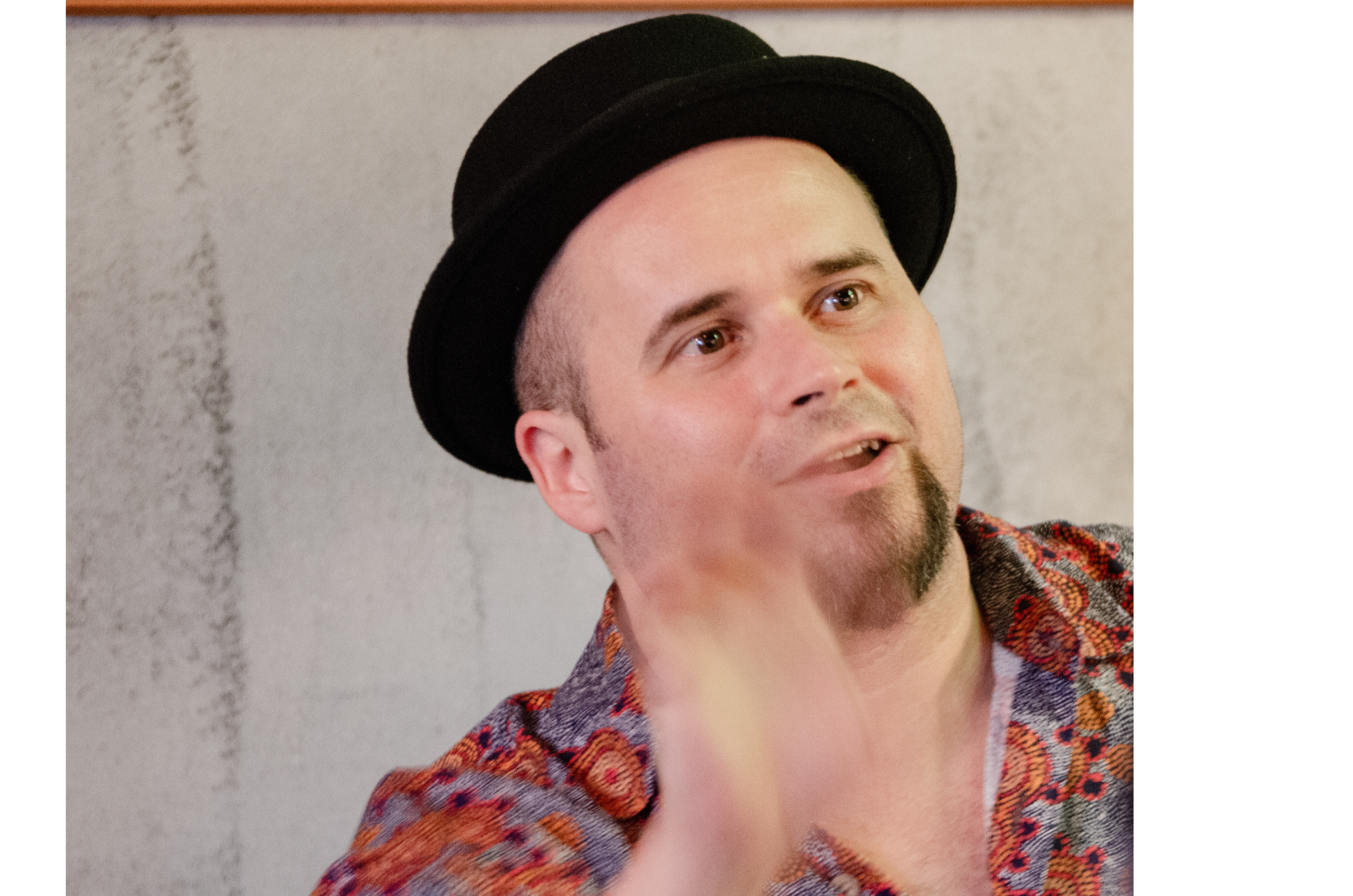 Singer wearing a black hat and patterned shirt, gesturing expressively