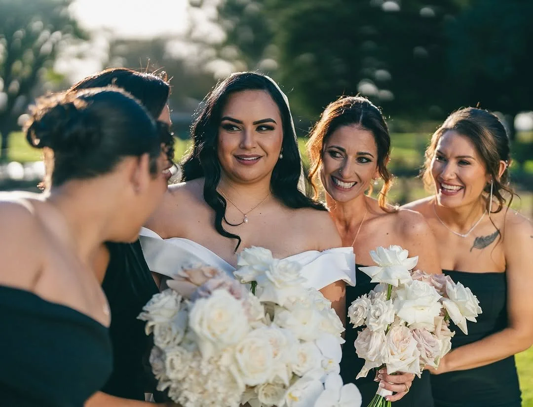 Women dressed in formal attire holding bouquets at an outdoor event.