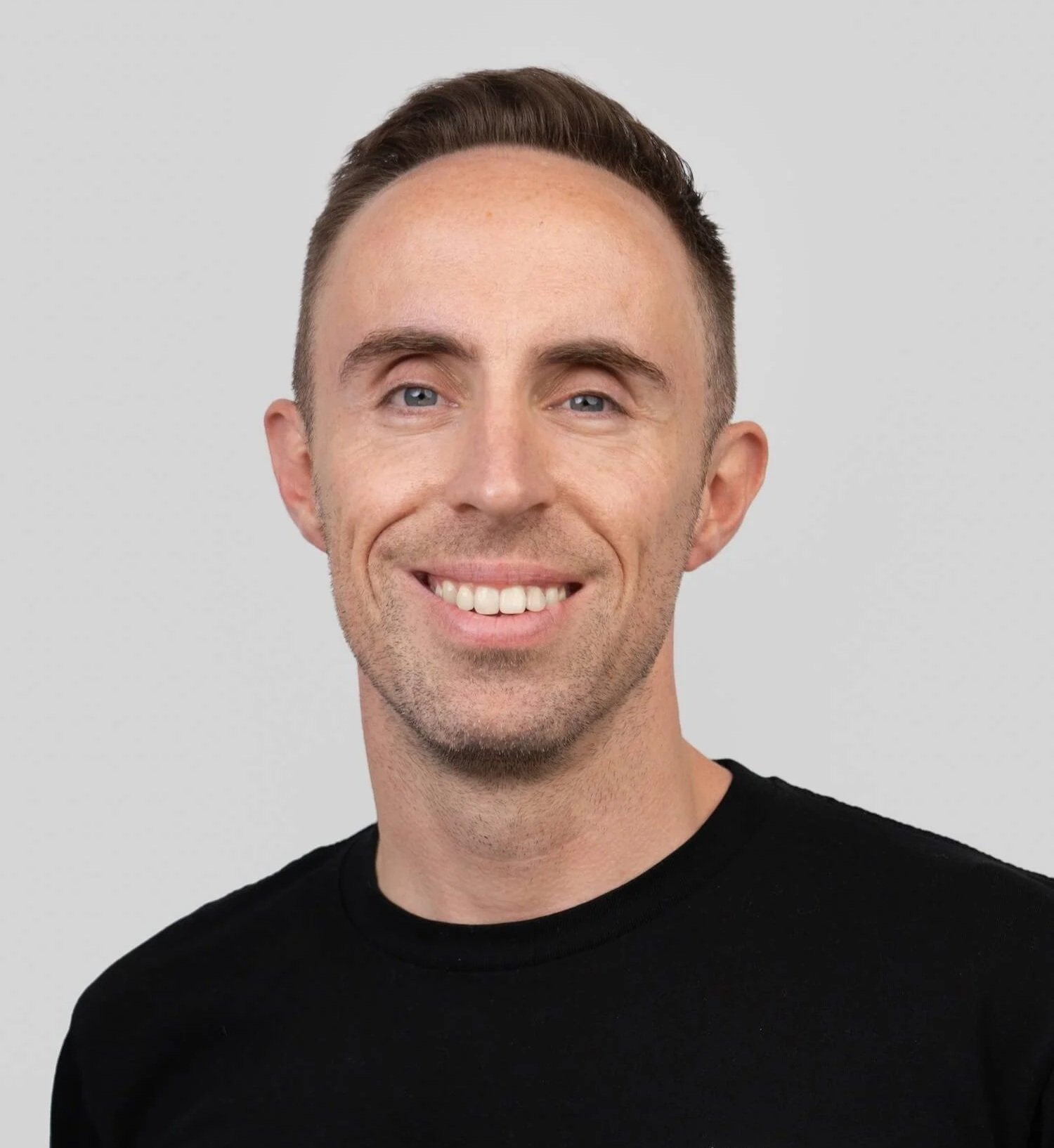 Smiling man with short brown hair wearing a black T-shirt with a TAS logo.