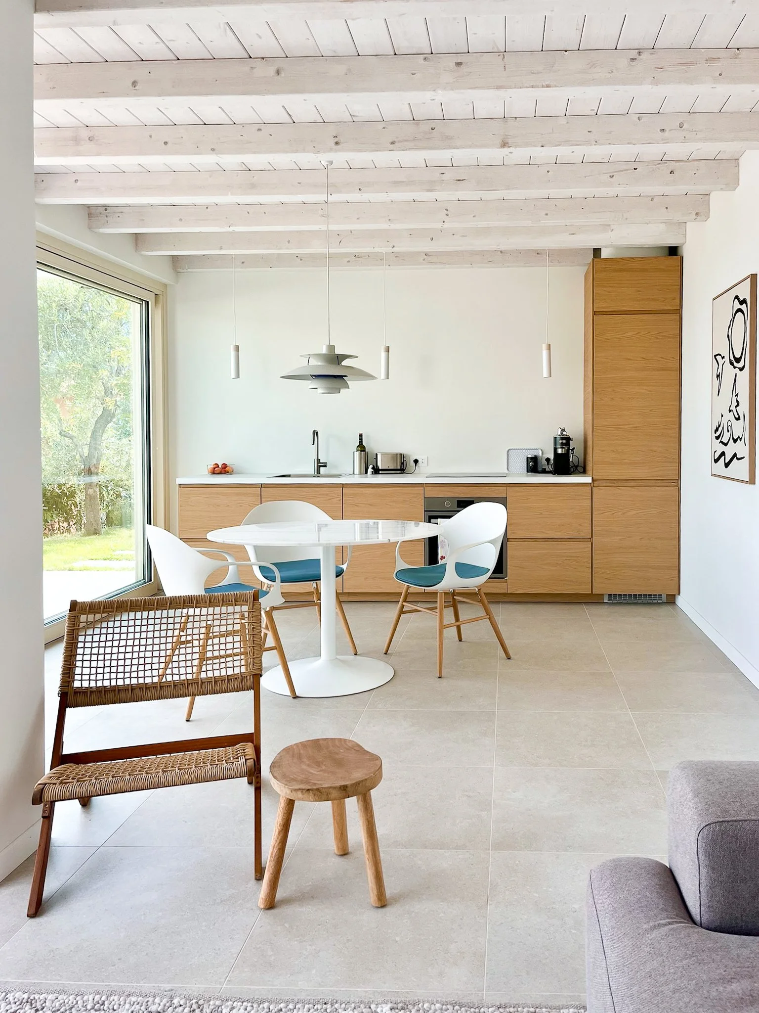 Moderner, heller Küchenbereich aus Eichenholz mit Esstisch, weißen Stühlen, großen Glasfenstern, Holzdecke und minimalistischer Dekoration.