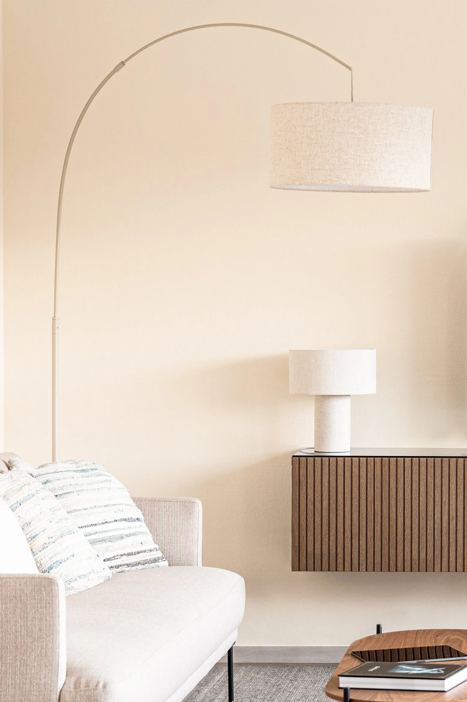 Innenraum mit Sofa, Kissen, Stehlampe und Seitenschrank in neutralen Tönen.