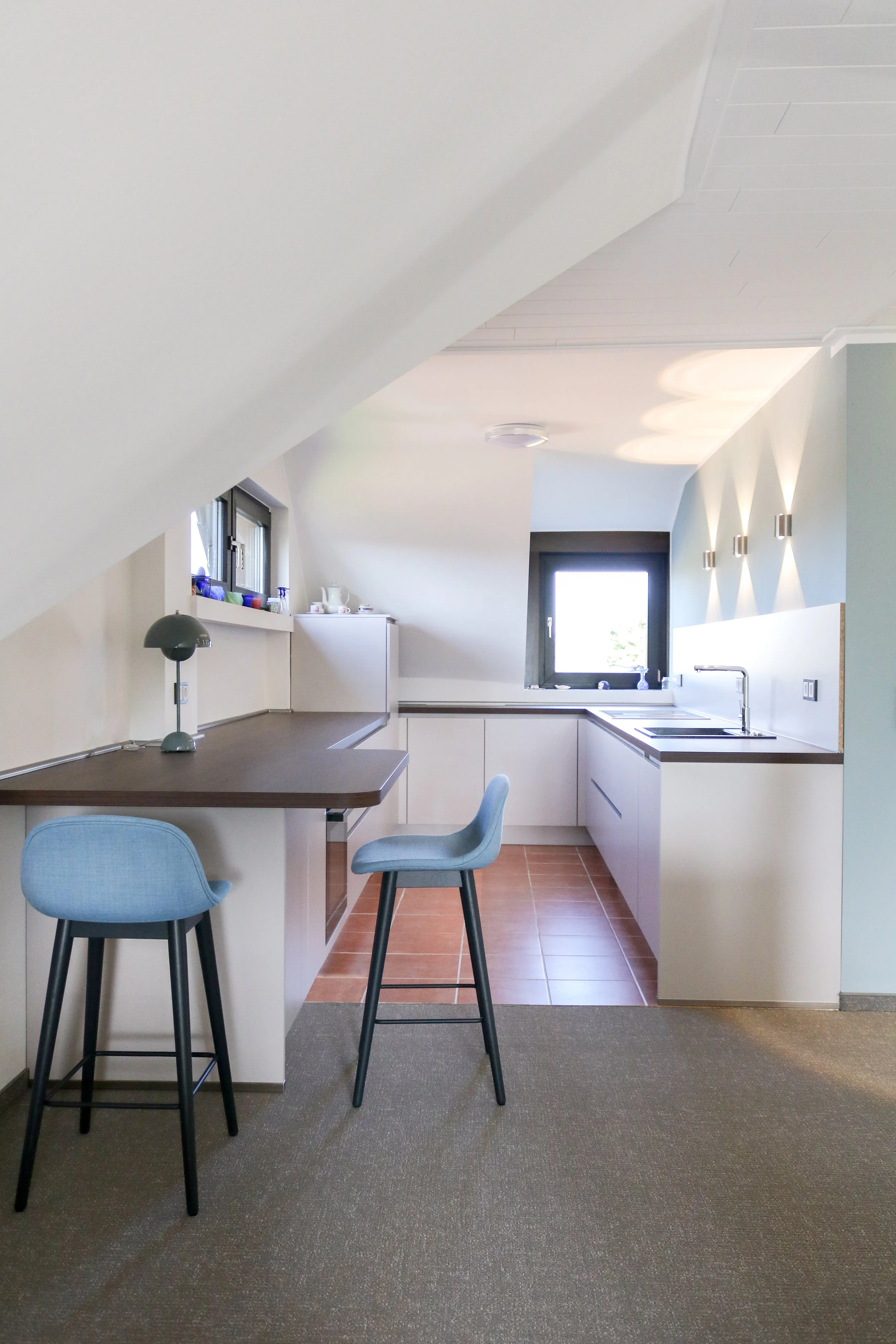 Moderne Küche mit Sessel und Barhockern in einem Dachgeschoss.