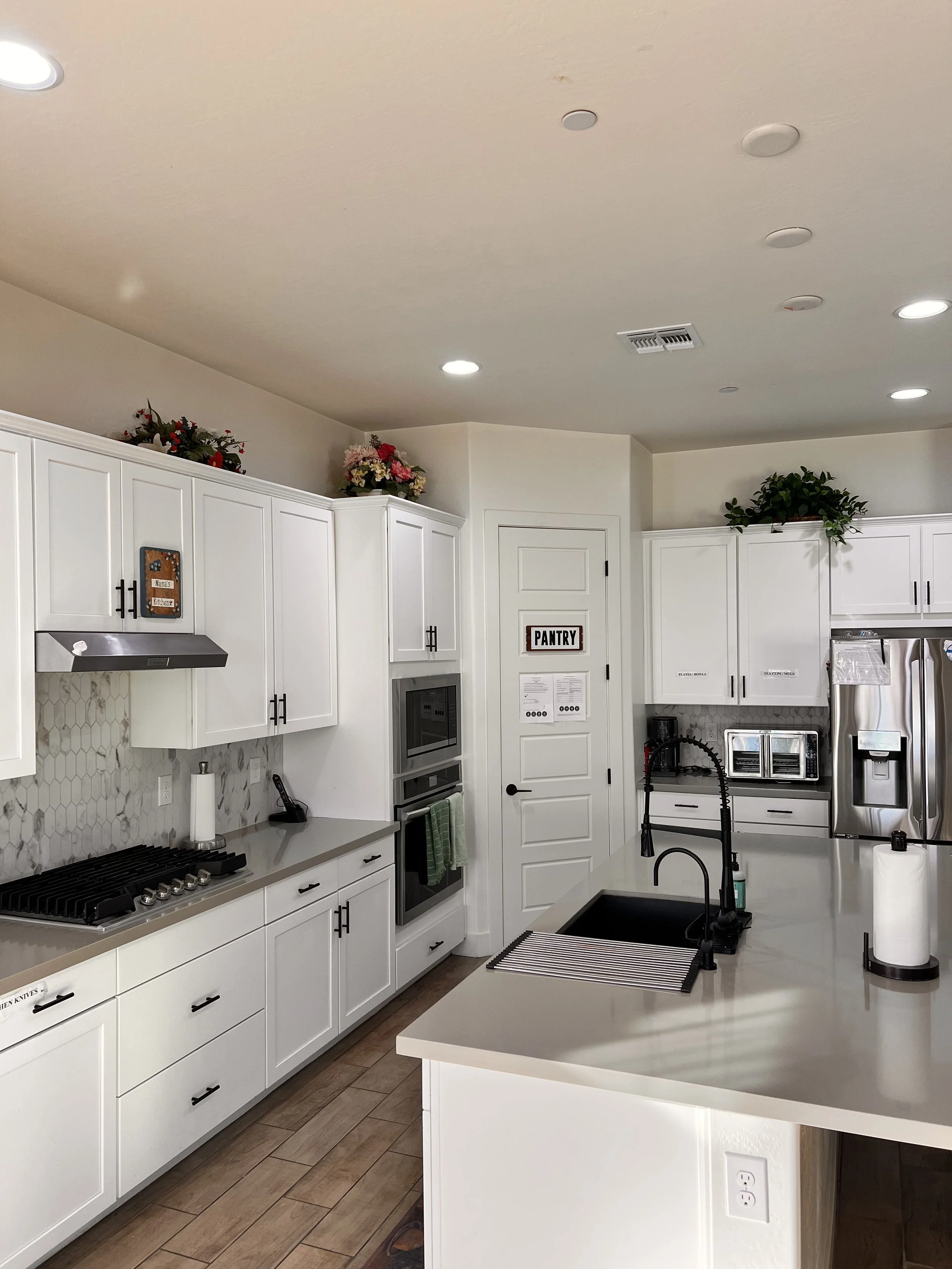 Modern kitchen with white cabinets, gray countertops, stainless steel appliances, and decorative greenery on top of cabinets.