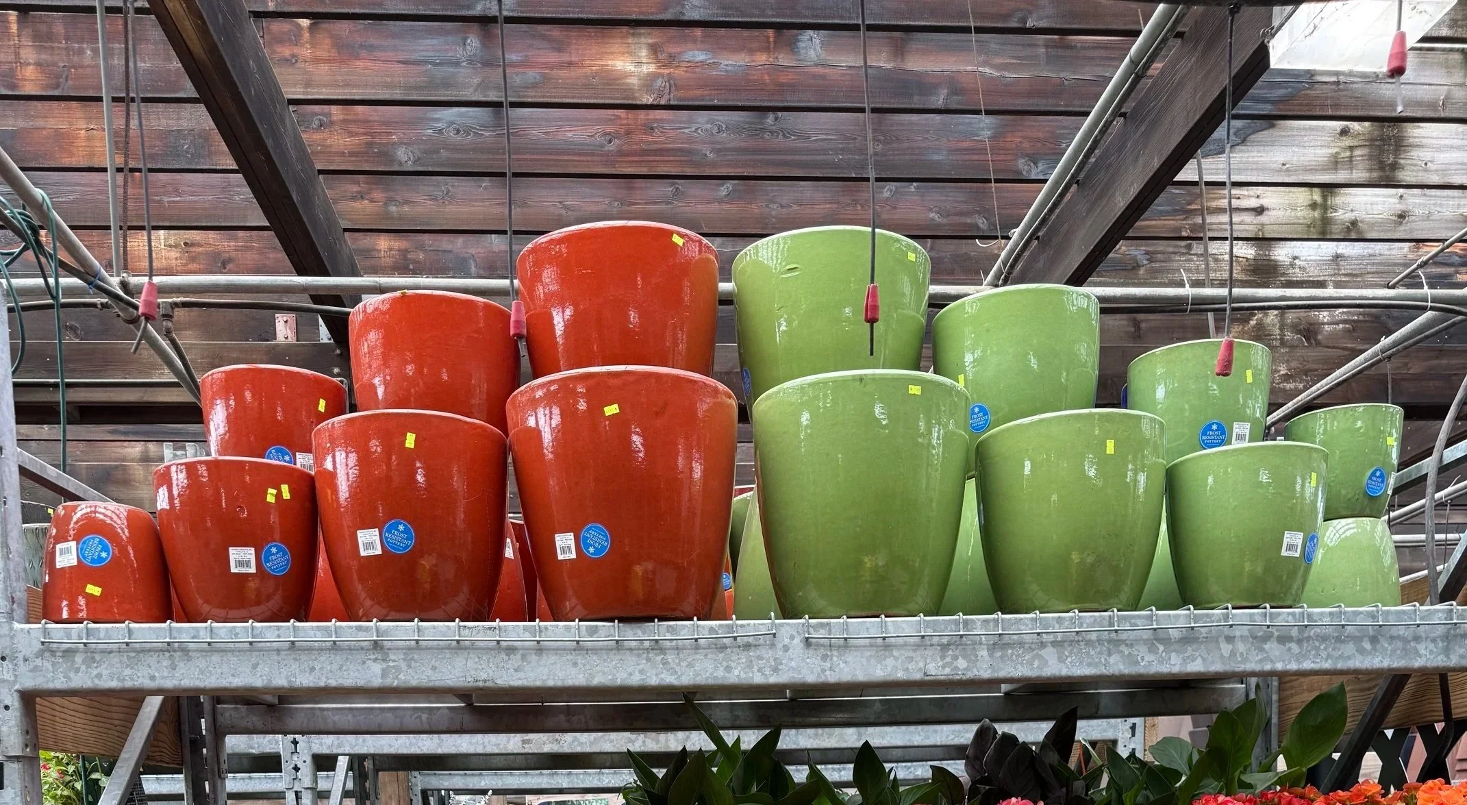 Multiple large orange and green plant pots stacked on a metal shelf at Allemon’s Landscape Center, Detroit, Michigan serving the Grosse Pointe, St. Clair Shores, and Detroit Communities since 1929.