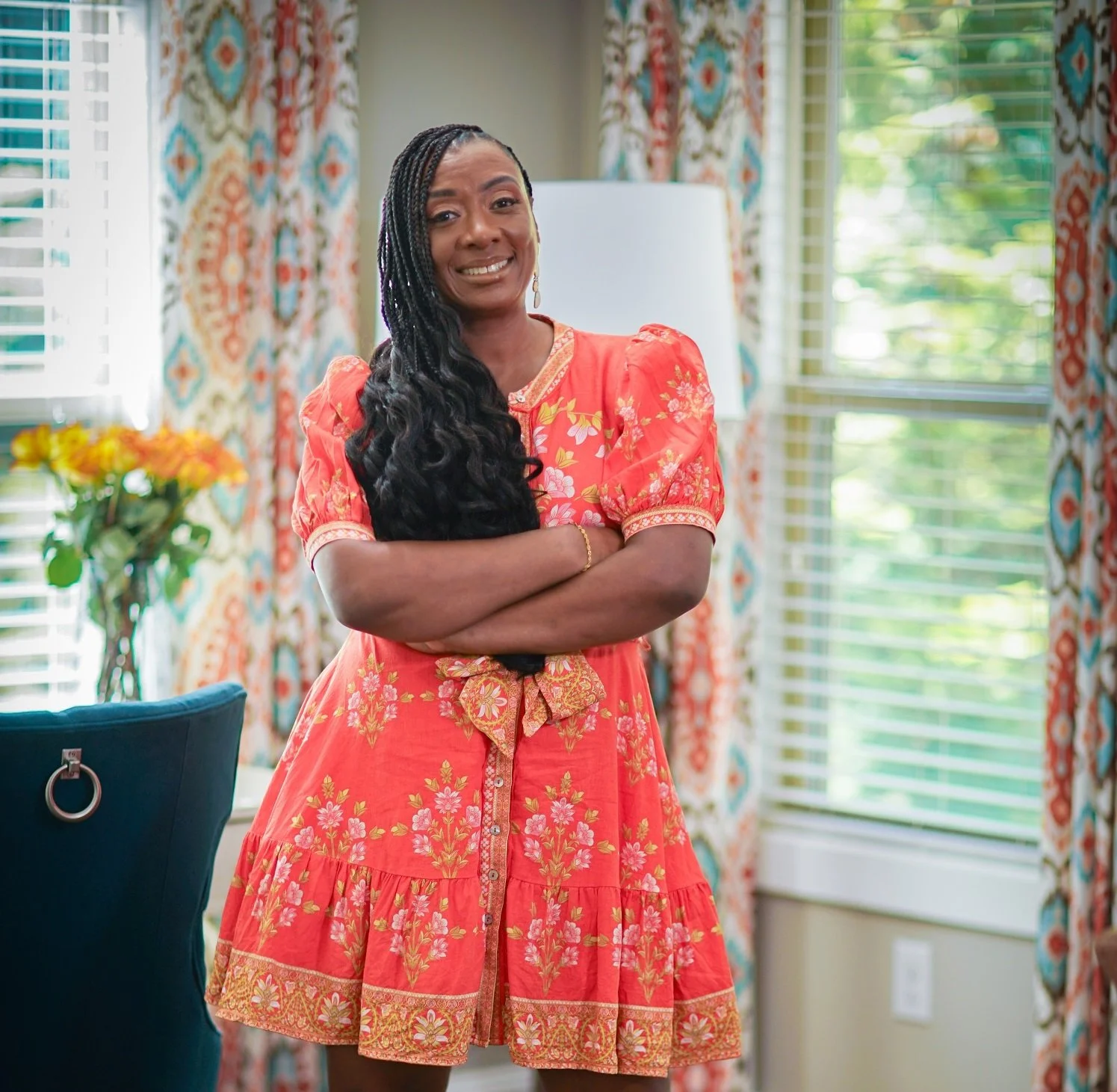 Sonia Foster, interior designer at Beyond Elegance Design, standing in colorful living room wearing coral floral dress