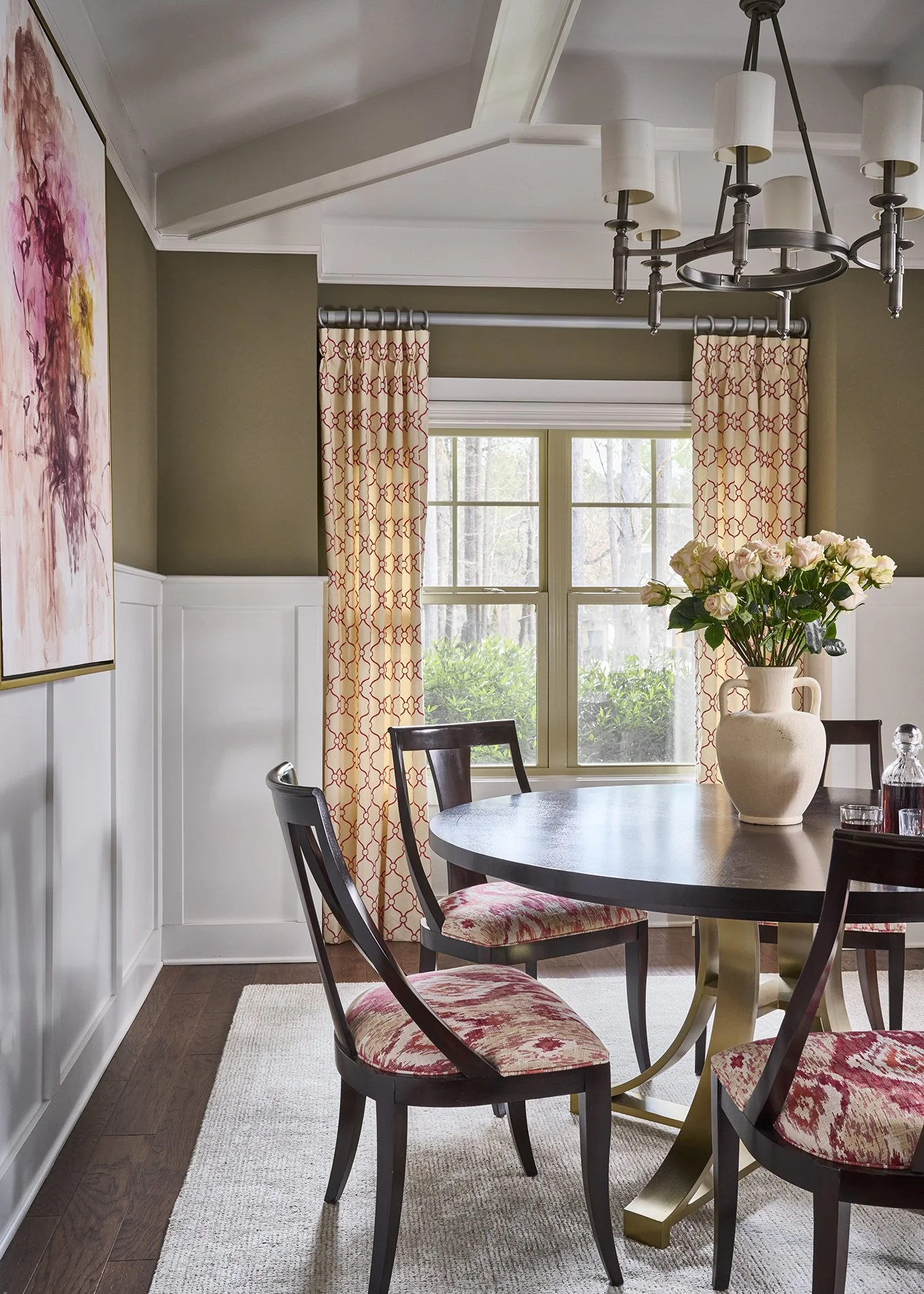 Formal dining room through arched entry with coffered ceiling, olive walls, abstract floral portrait, round pedestal table, and klismos chairs