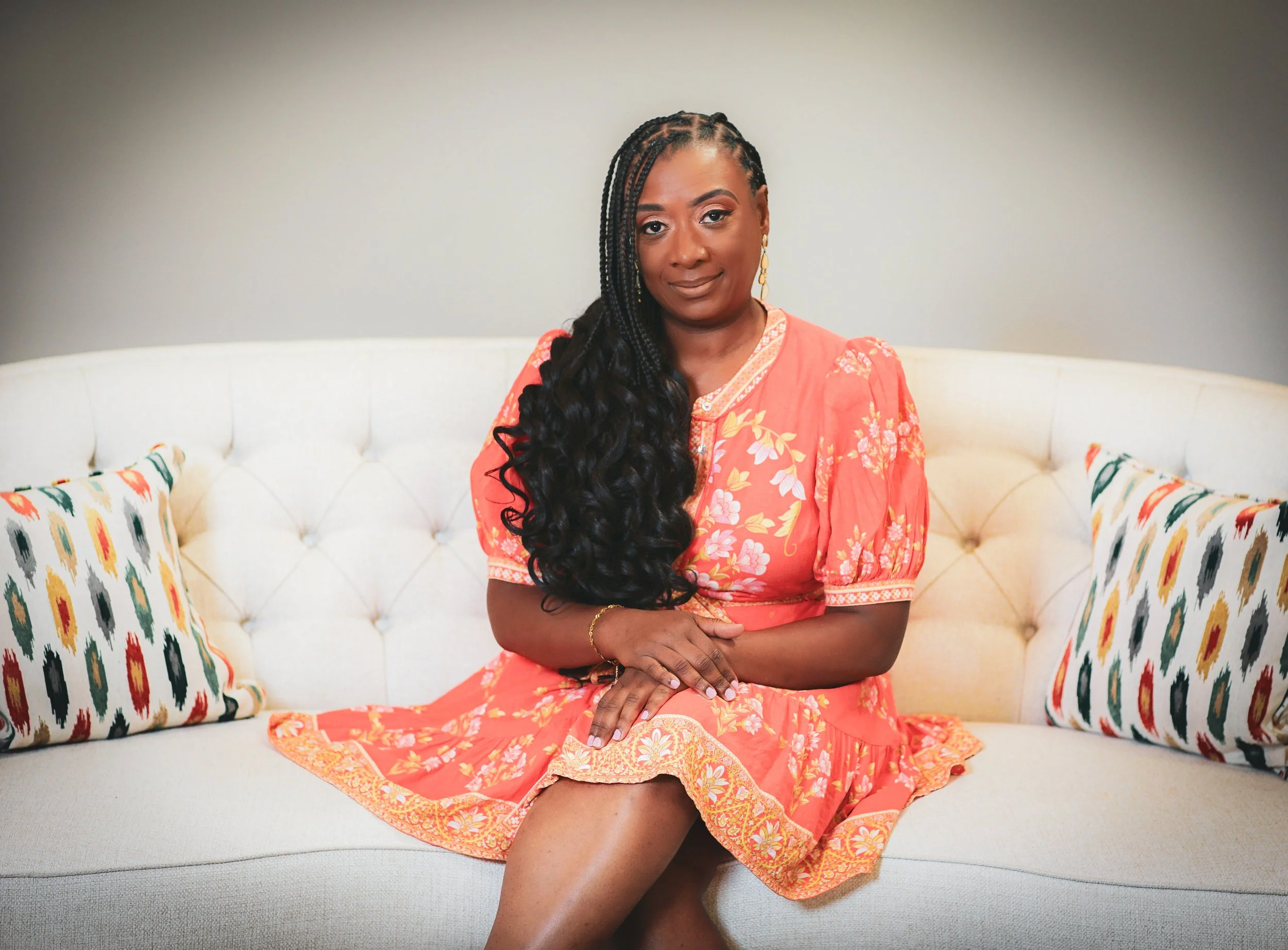 Sonia Foster, interior designer at Beyond Elegance Design, sitting on a white couch wearing coral floral dress