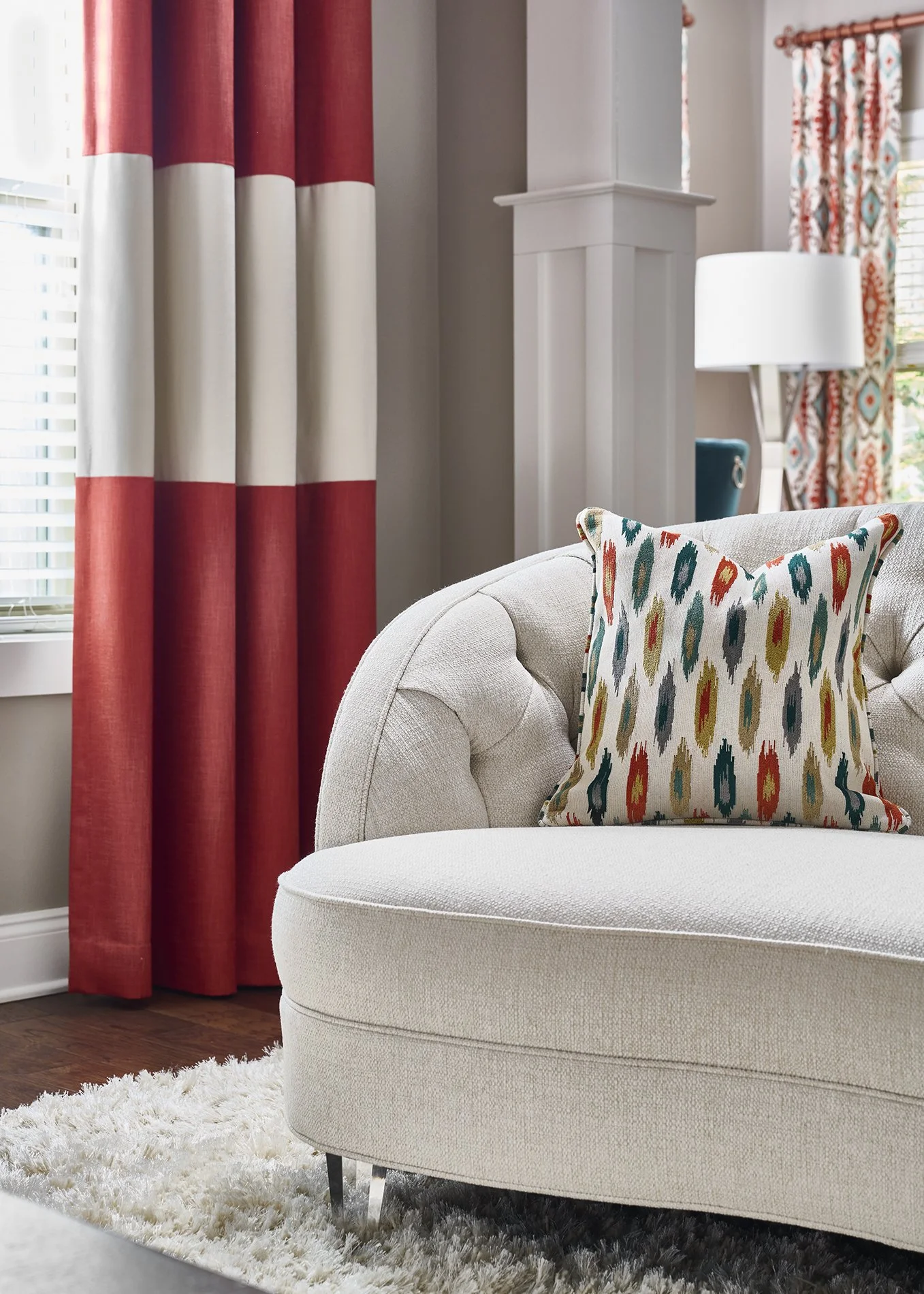 Cream tufted curved sofa with ikat accent pillow and orange and cream color-blocked drapes