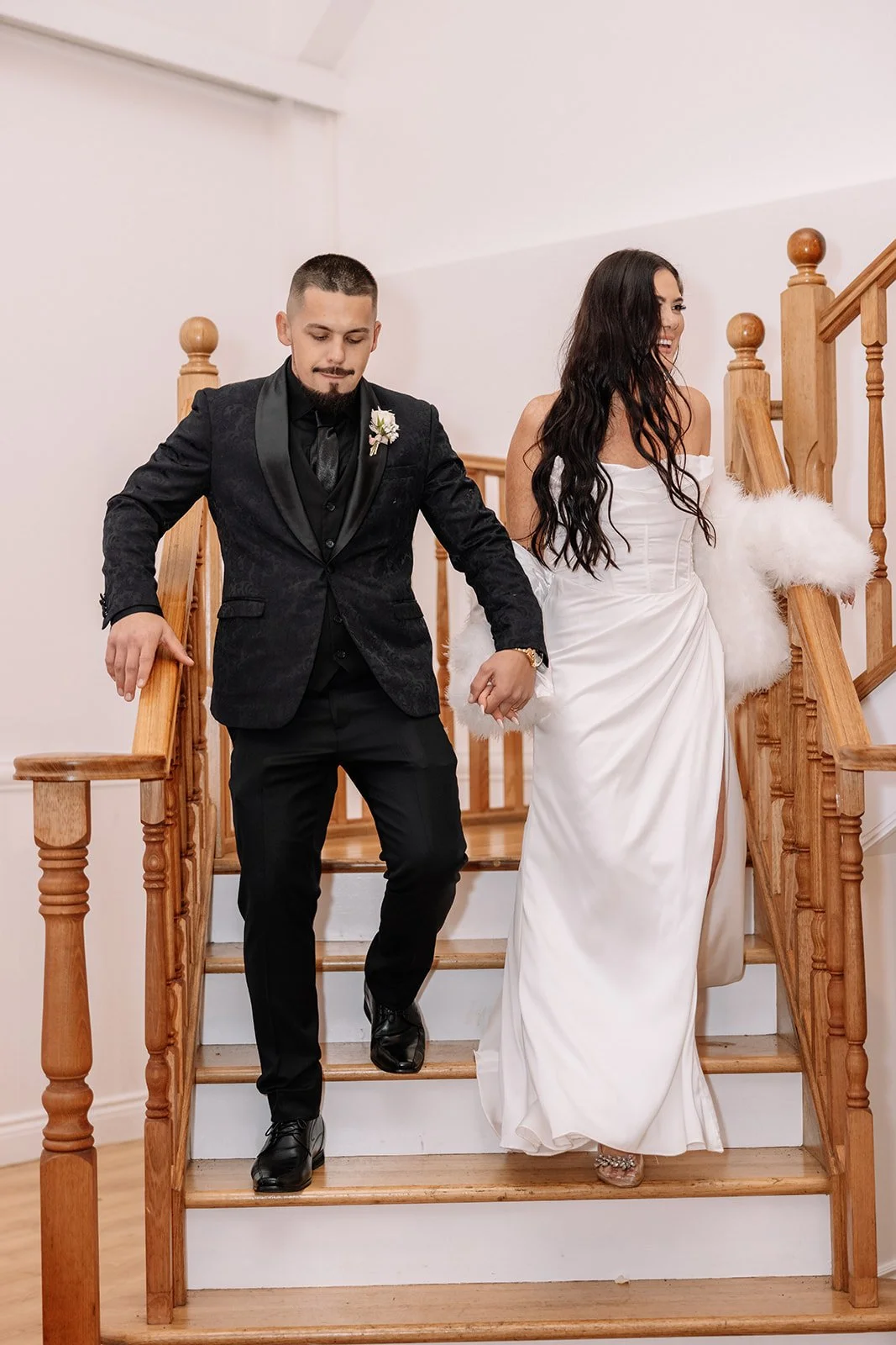 A bride wearing a white gown and a soft white wrap beside her partner on a staircase