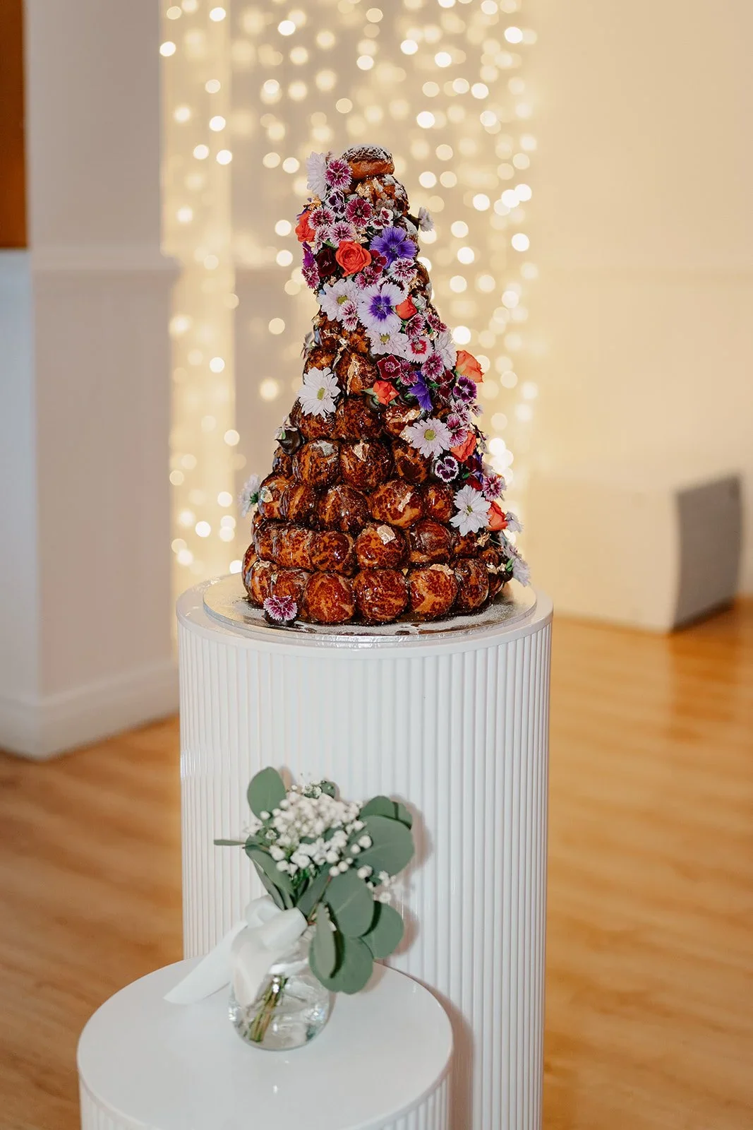 A croquembouche decorated with colourful flowers on a wedding dessert plinth