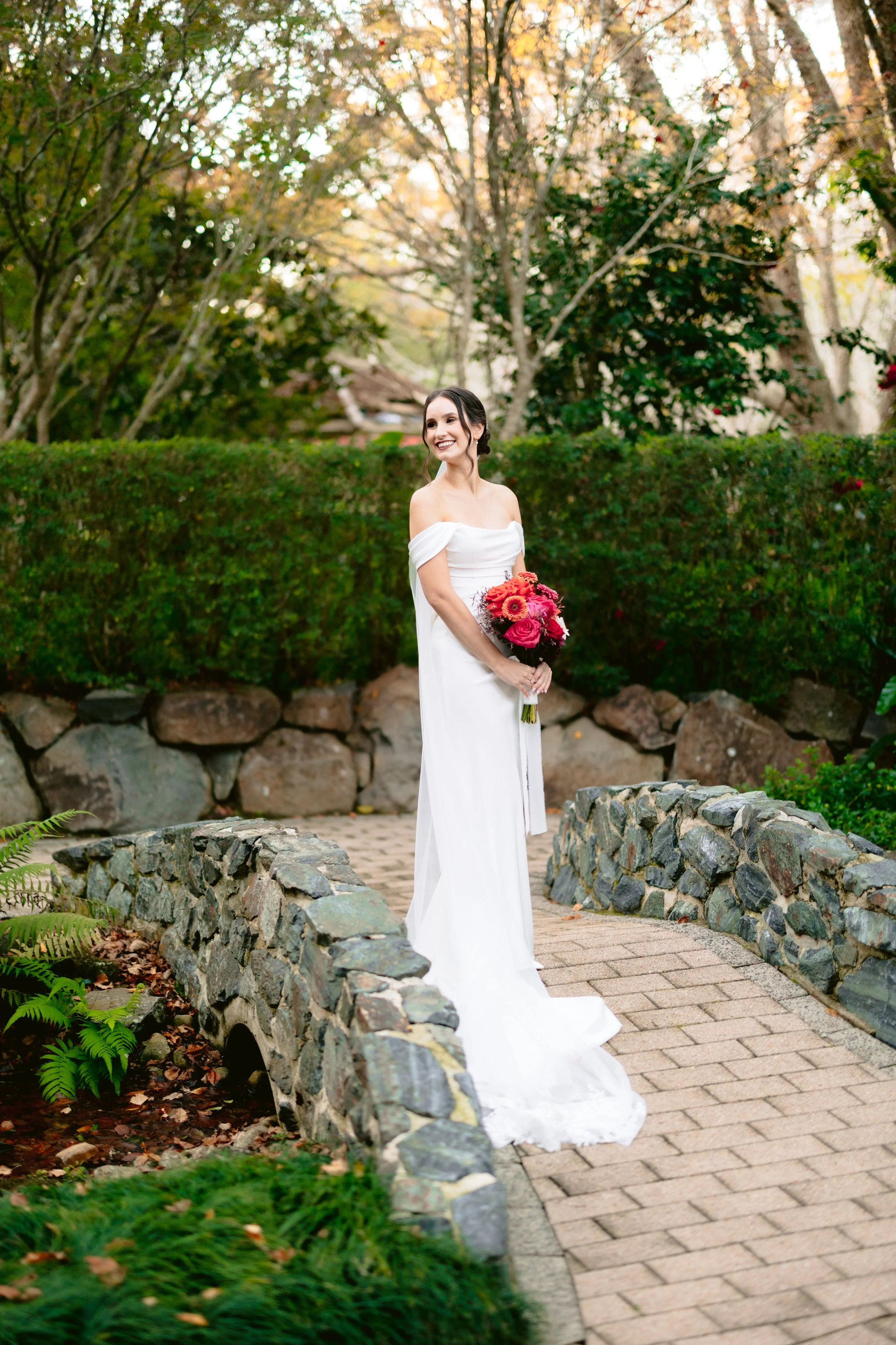 A bride holding a colourful bouquet on the stone garden bridge at Shambala Estate, Tamborine Mountain.