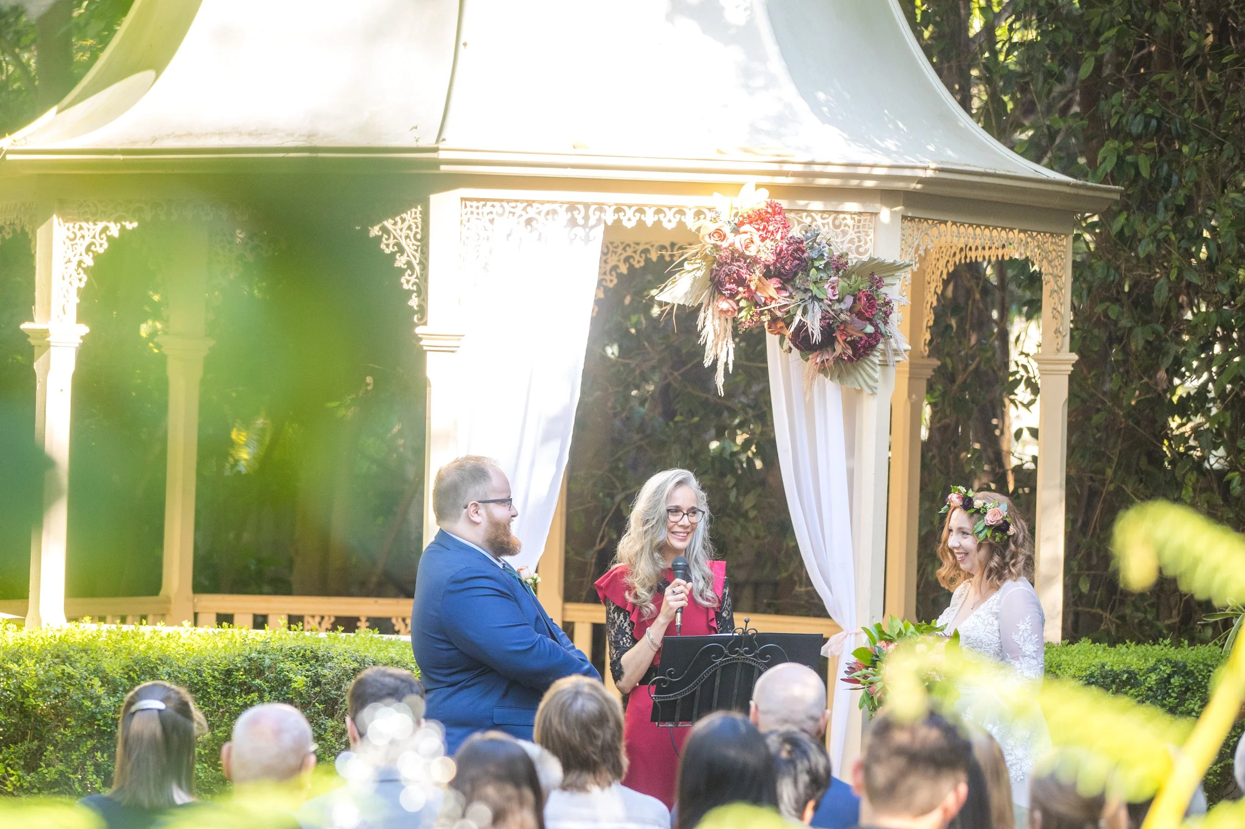 Tara Chapman addressing guests as celebrant beneath the garden gazebo during Christina and Thomas Murray’s wedding at Shambala Estate.