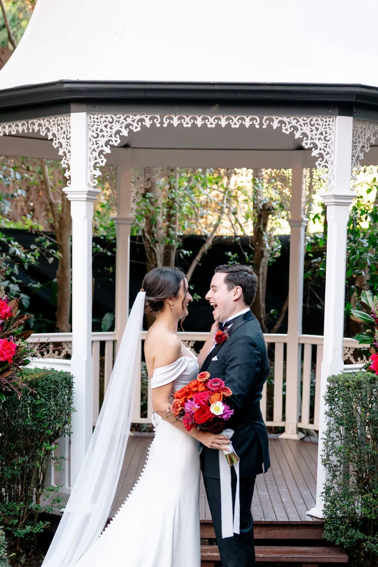 A newlywed couple smiling together beside the garden gazebo at Shambala Estate