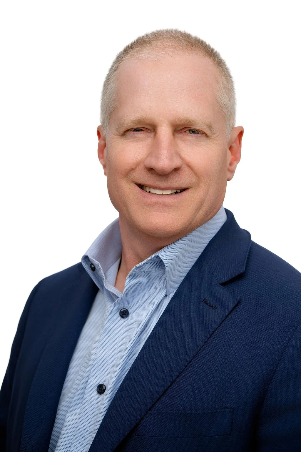 Headshot of a smiling man wearing a blue suit jacket and a light blue collared shirt, against a white background.