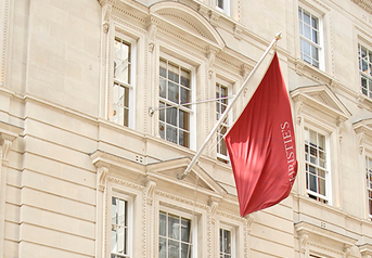 Red flag with white text hanging outside a beige building with multiple windows.