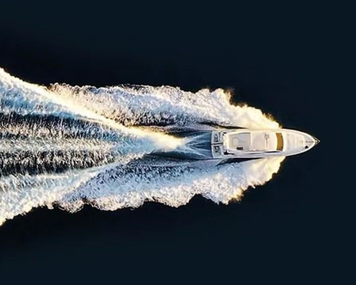 A white motorboat speeding across dark water, creating a large trail of white wake behind it.