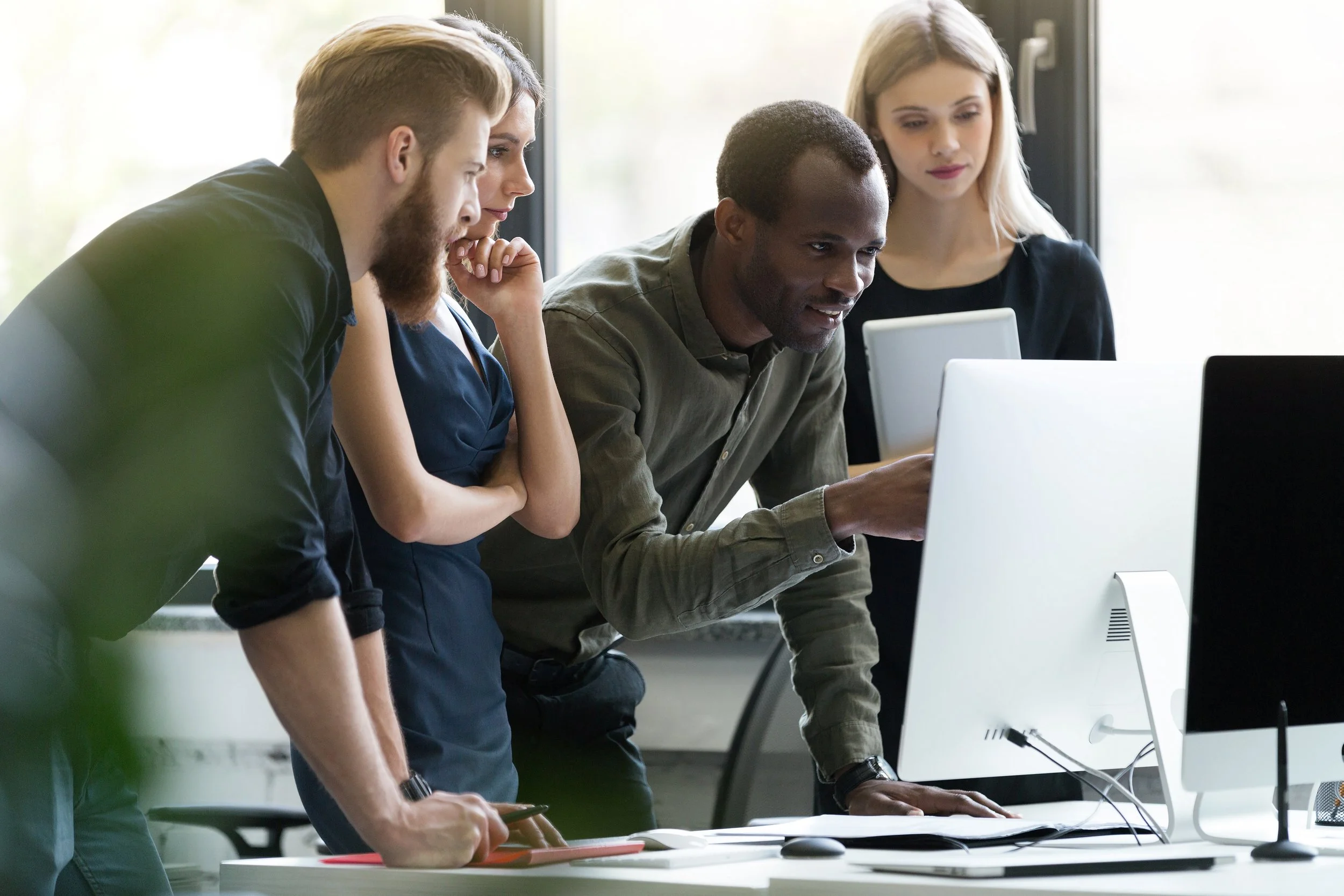 Five diverse coworkers gathered around a computer, collaborating in a modern office.