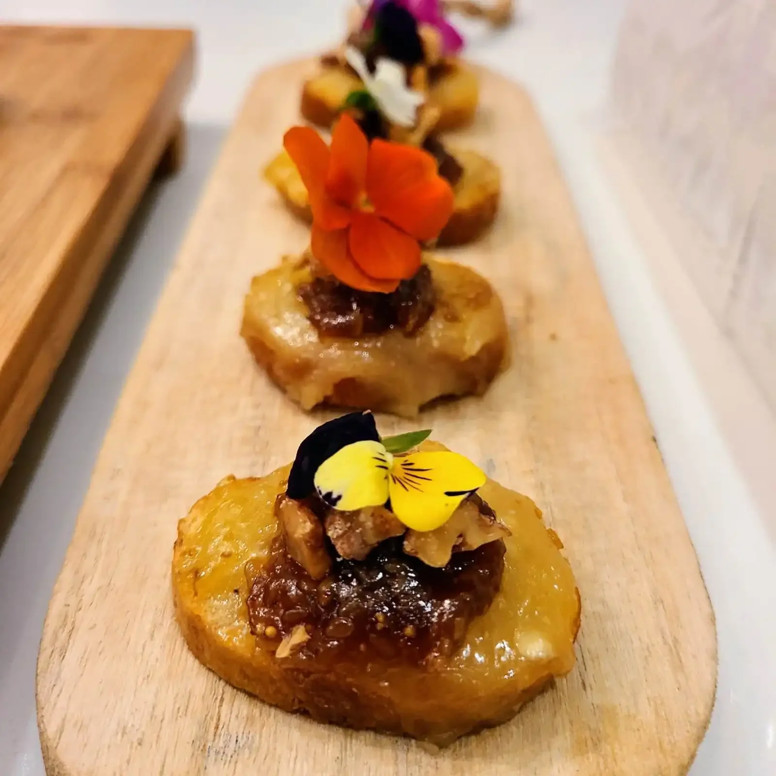 Tartines décoratives garnies de divers ingrédients, avec des fleurs comestibles, présentées sur une planche en bois.