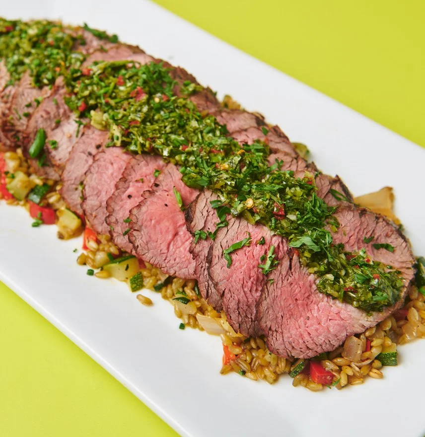 Boeuf rôti tranché avec une sauce verte sur un lit de riz sauté aux légumes, présenté sur une assiette blanche.