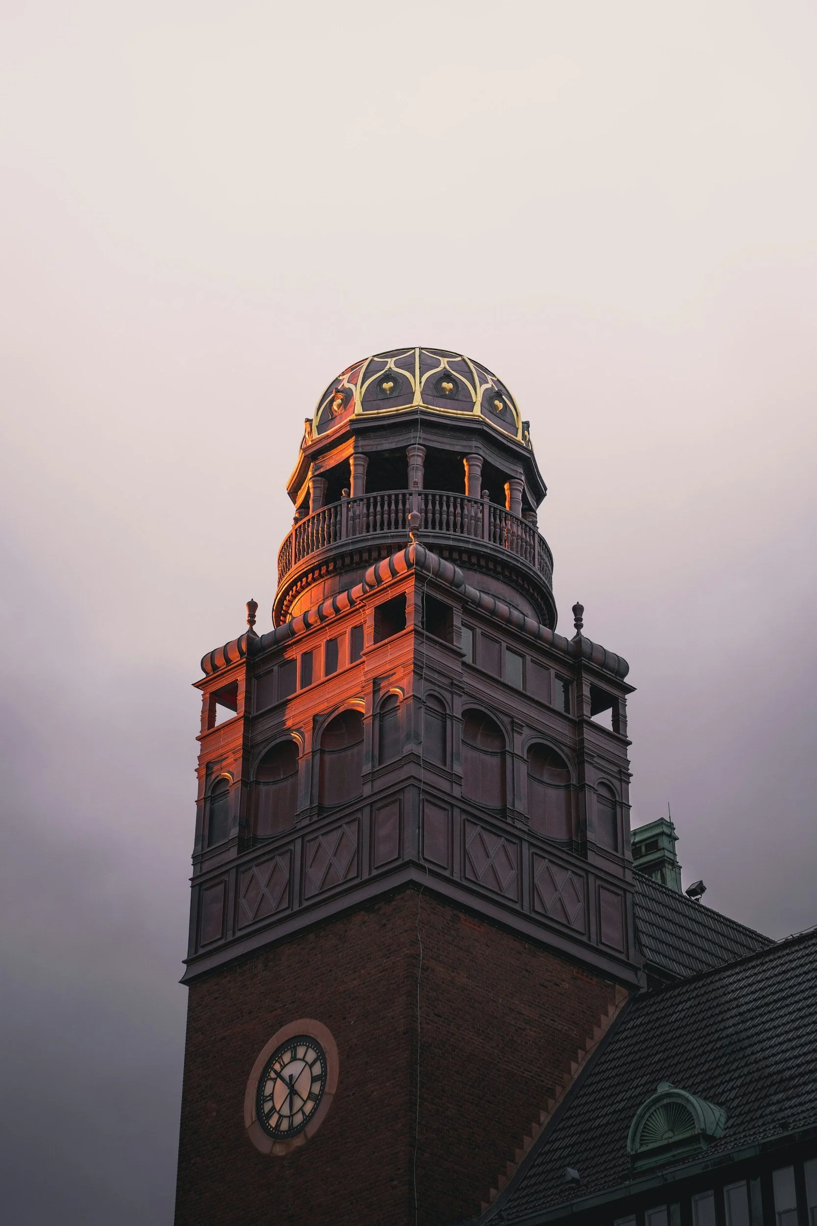 Ornate historic brick clock tower with a domed cupola against a cloudy evening sky