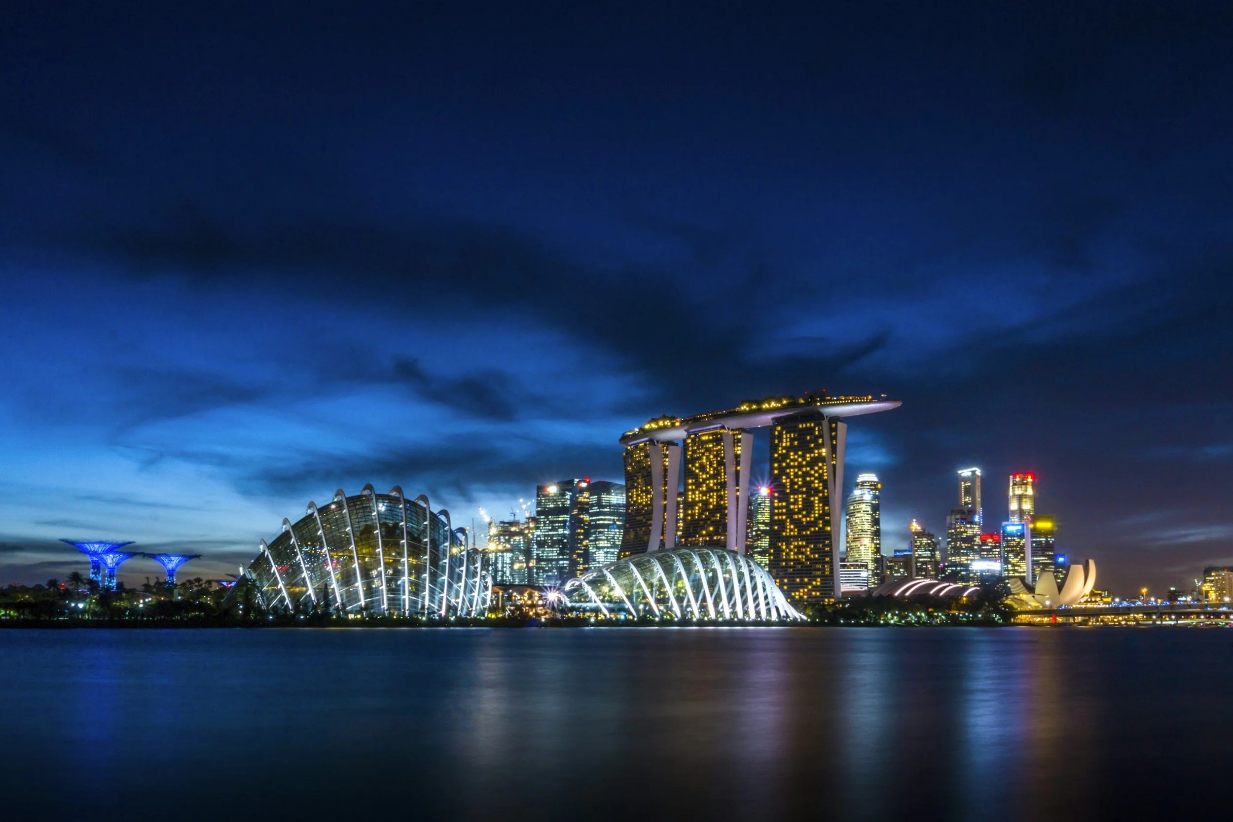 Night view of Singapore skyline featuring Marina Bay Sands hotel, artscience Museum, and skyscrapers reflected on the water.