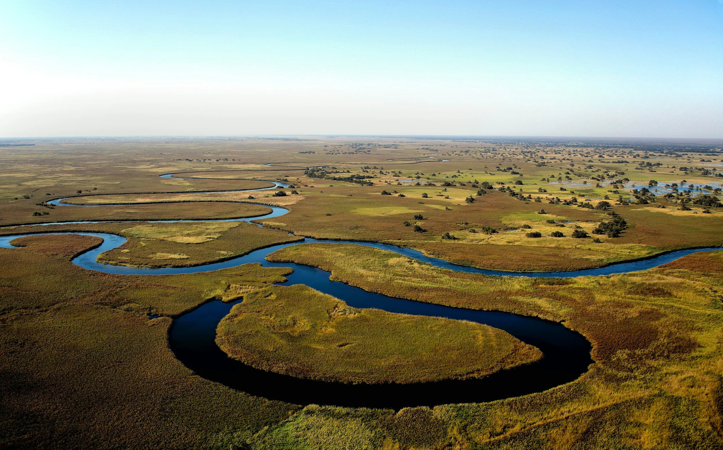 A winding river flows through a flat, grassy landscape with scattered trees.