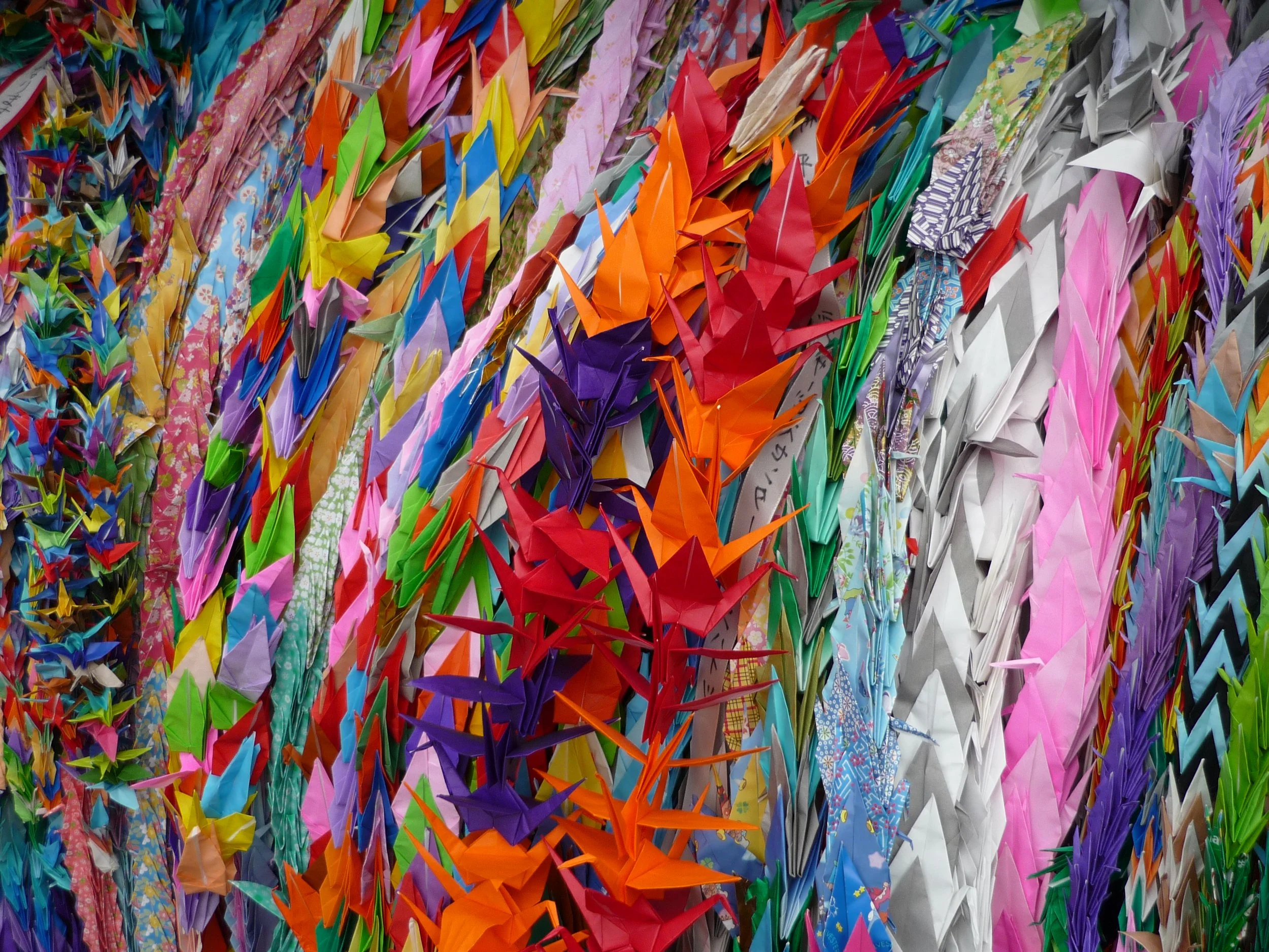 A colorful display of numerous paper origami cranes arranged in rows, featuring various colors and patterned paper.
