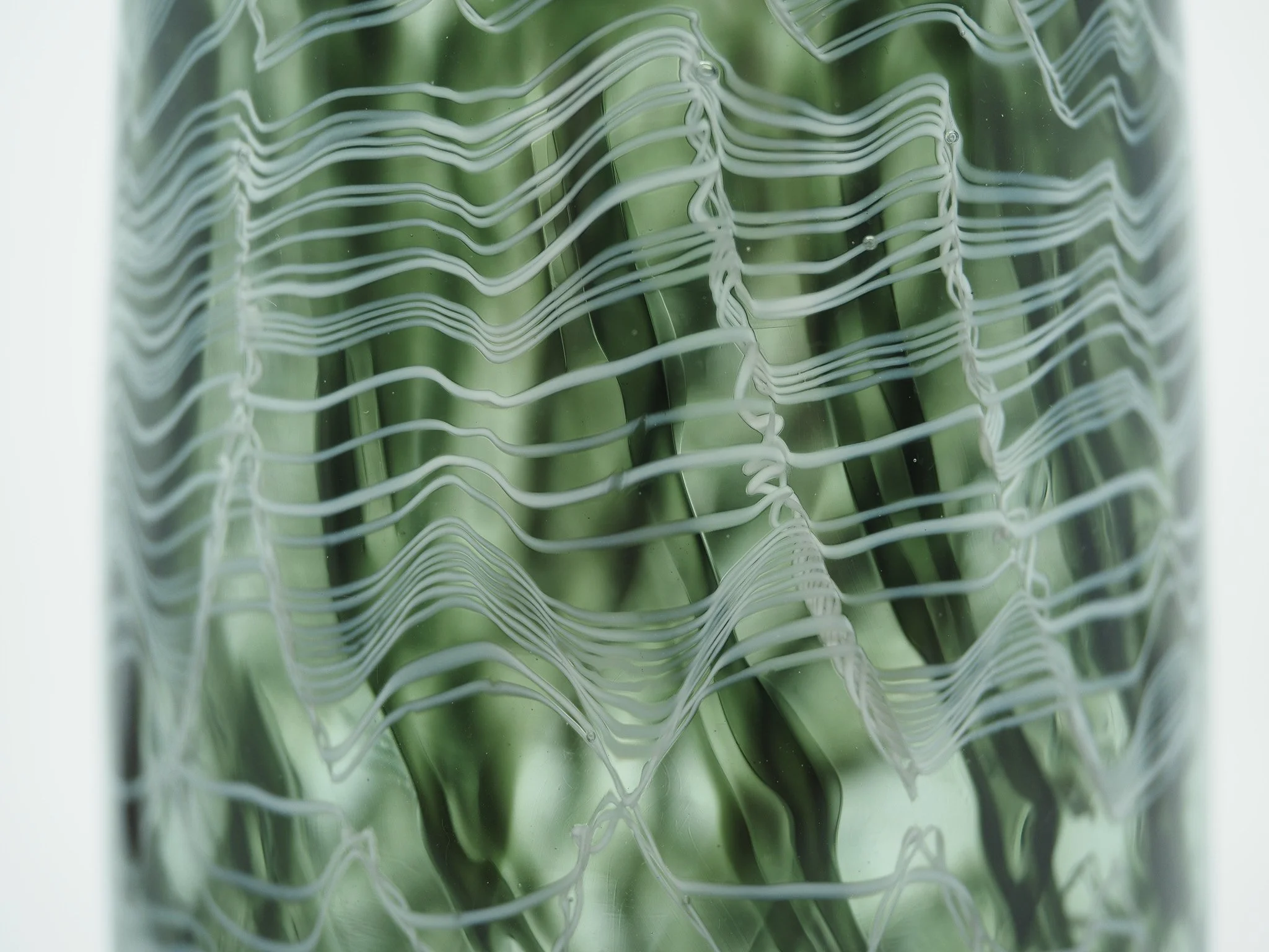 Nahaufnahme einer Glasvase mit grünem Blatt, das durch ein Muster aus weißen Linien sichtbar ist.