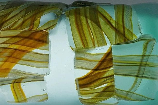 Bunte gebrochene Glasstücke mit gelben, braunen und grünen Linien, auf Lichtgrund.