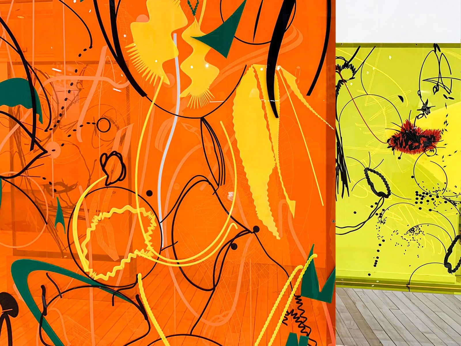 Two colorful abstract paintings with swirling lines, shapes, and splashes of color displayed on walls in an art gallery.