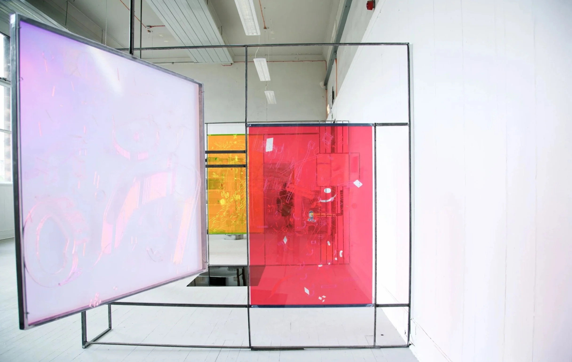 An art installation of multiple transparent, colored panels in a gallery space, with a large pink panel, a yellow panel, and a purple panel, all framed in black metal.