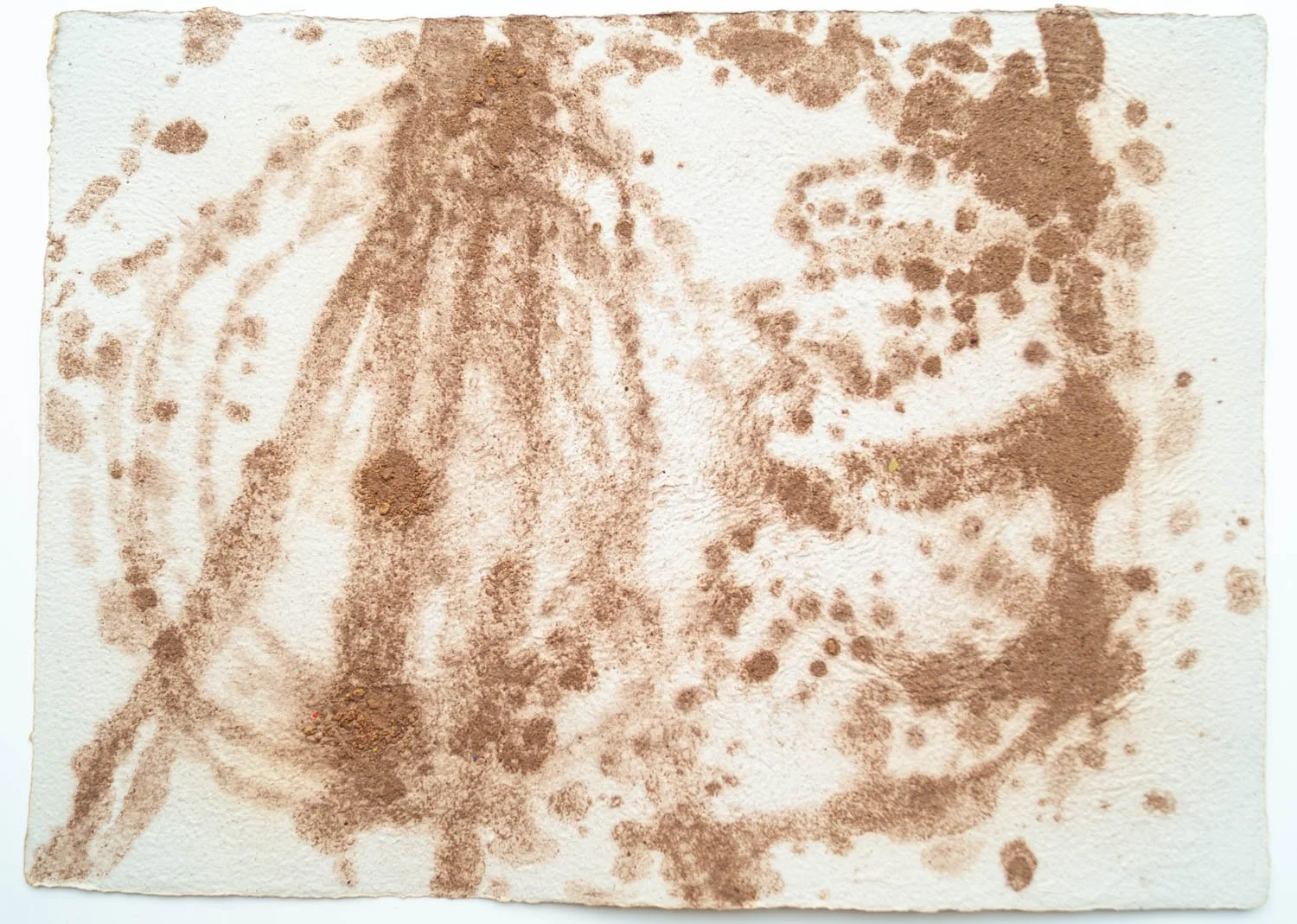 A photograph of a textured paper with brown watercolor or ink abstract patterns, resembling a stylized face or human portrait with a prominent nose and eyes.