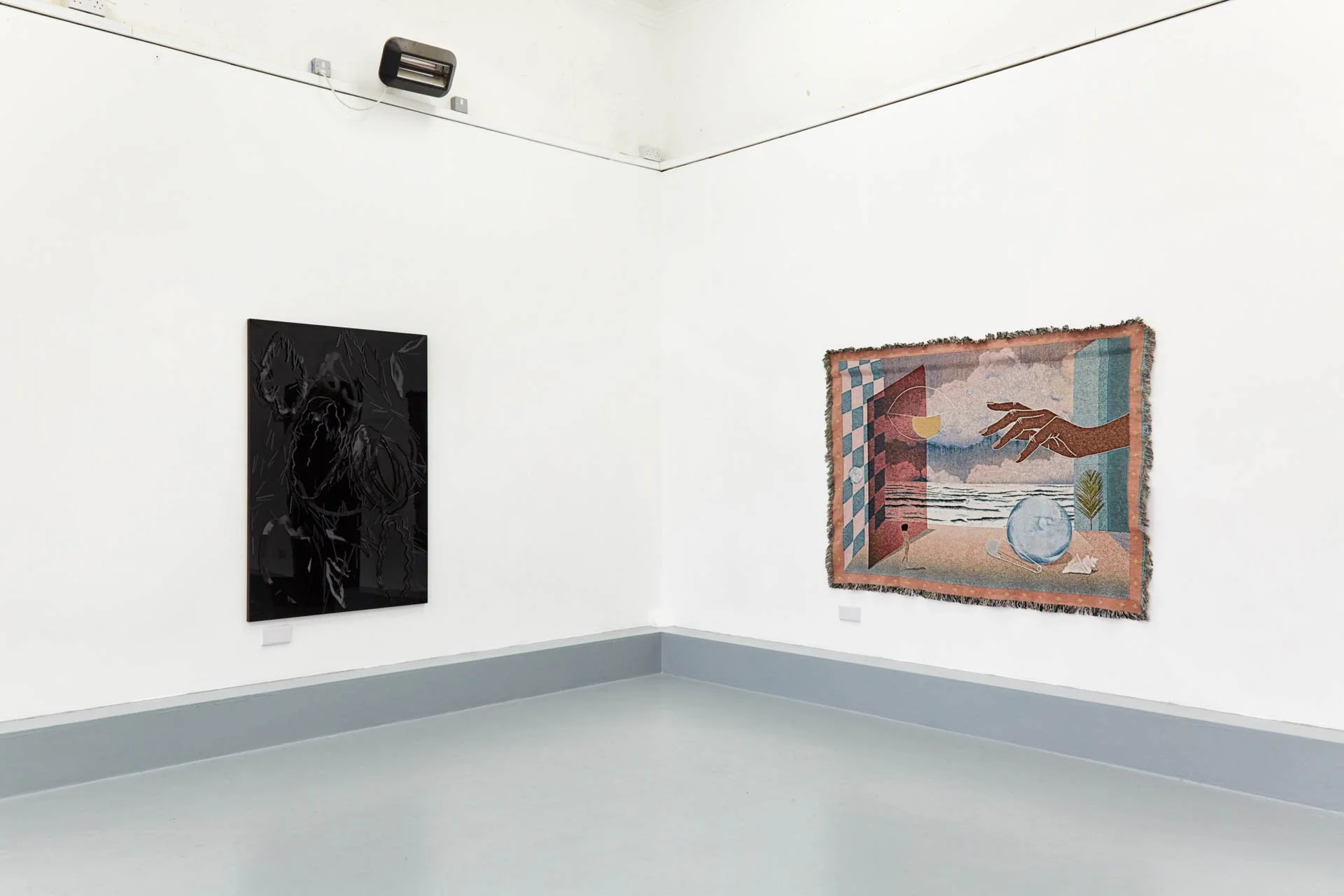 An art gallery with white walls, showcasing two paintings: one abstract black painting on the left and a colorful surrealist painting on the right featuring a hand, a drink, and a beach scene.