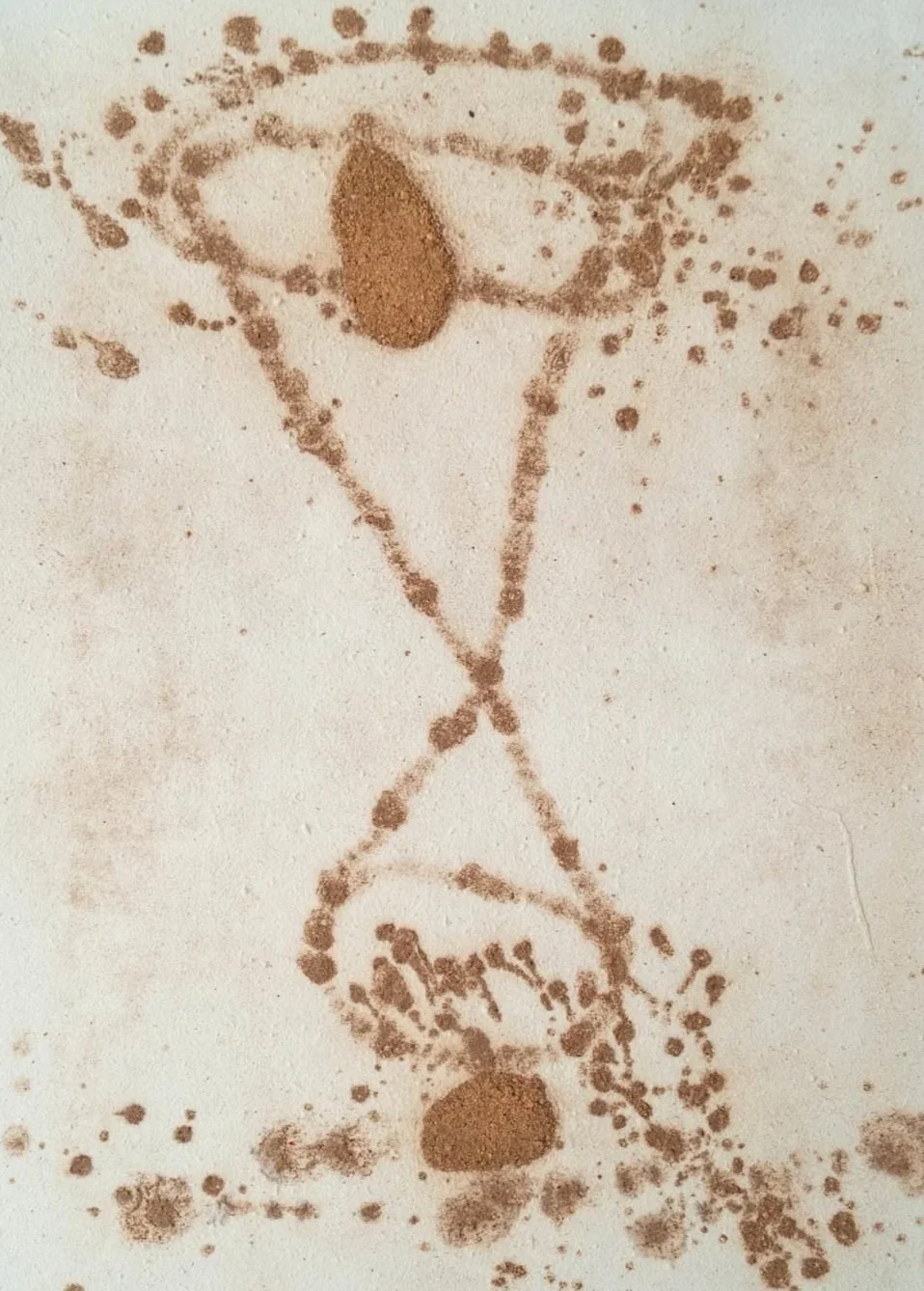 A drawing of a scientist with glasses and a lab coat, holding a beaker, made with brown cinnamon powder on a white surface.