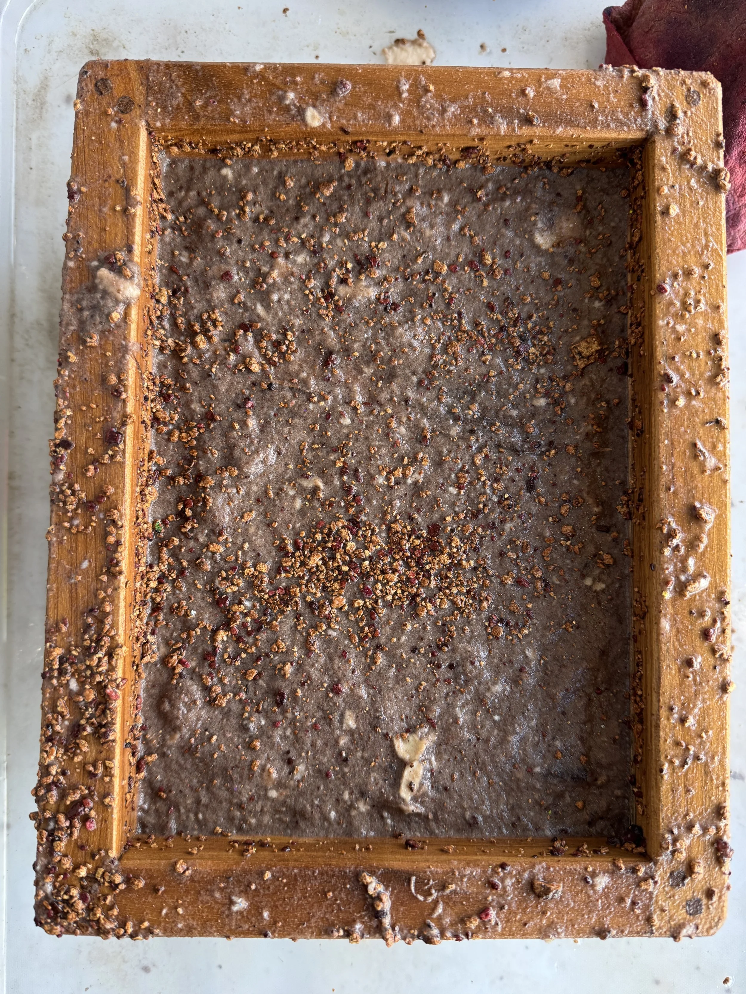 Top view of a rectangular wooden frame filled with a mixture of mud, small rocks, and gravel, with some scattered gravel on the surface.